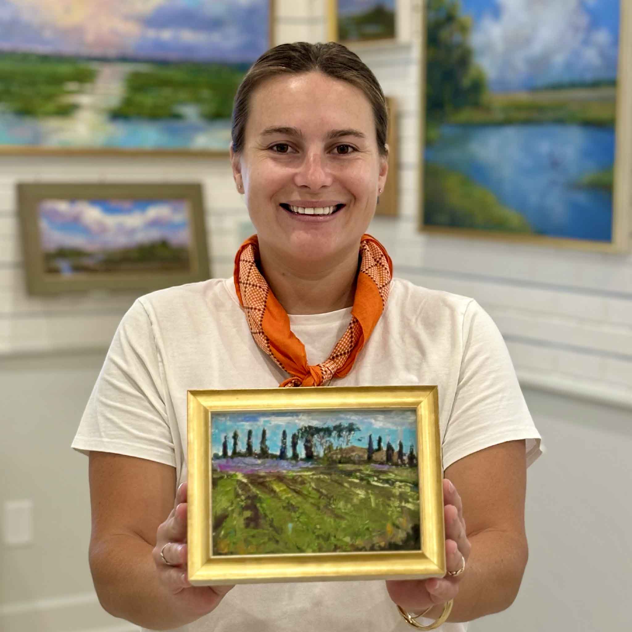 Gray Man Gallery team member Kyra holding Tuscan Summer by Jeanne O'Neal to show scale, an original Tuscany landscape oil painting featuring cypress trees, lavender fields, and rolling Italian countryside.