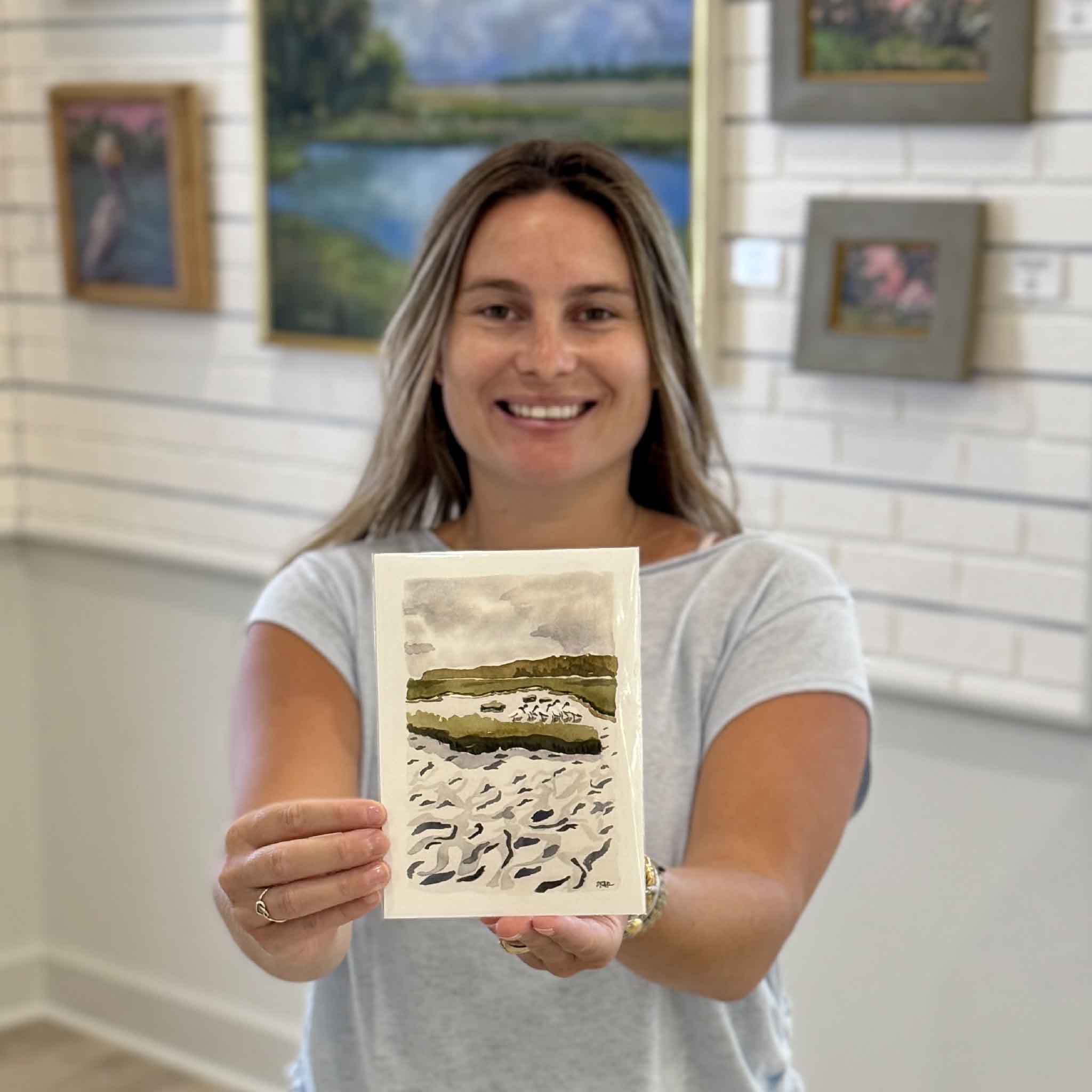 Kyra holding Woodstorks at the Horseshoe, a 5x7 Lowcountry marsh print by local artist Maggie Pelton featuring wood storks along a tidal creek. Available at Gray Man Gallery in Pawleys Island, South Carolina.