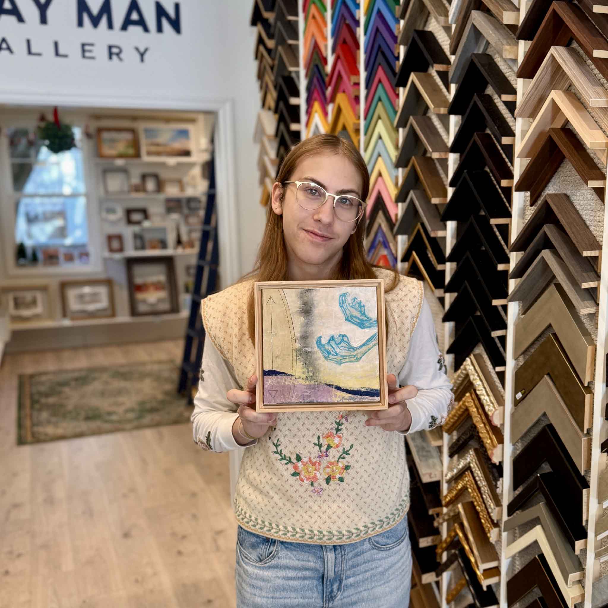 GMG team member holding Laurie McIntosh’s 5A mixed-media artwork to show scale and framed presentation.