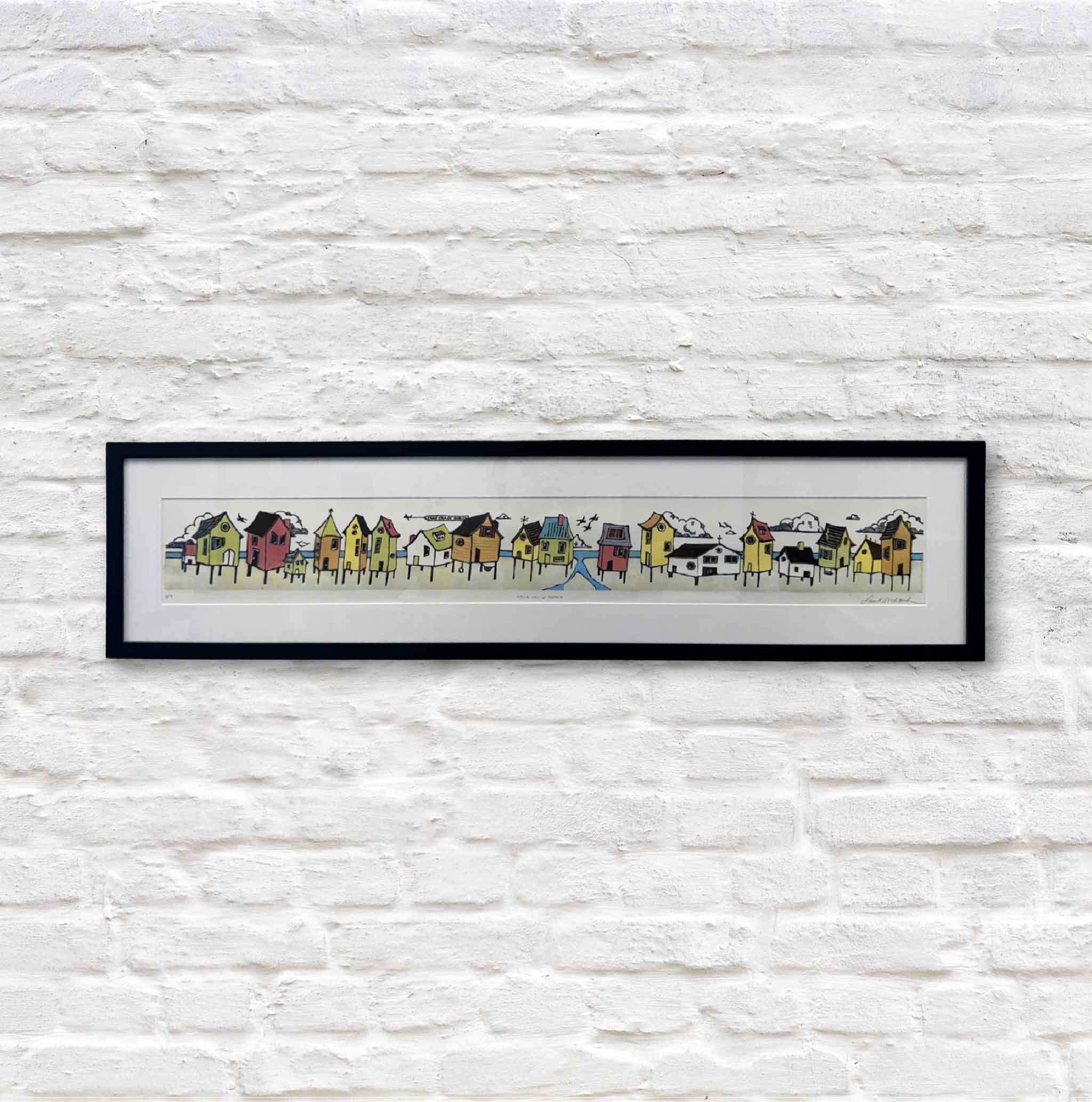 Stick House Beach, an original hand-pulled linocut reduction print by Laurie McIntosh featuring a whimsical row of colorful stilted beach cottages, birds overhead, and playful Lowcountry coastal charm. Framed artwork available at Gray Man Gallery in Pawleys Island, South Carolina.