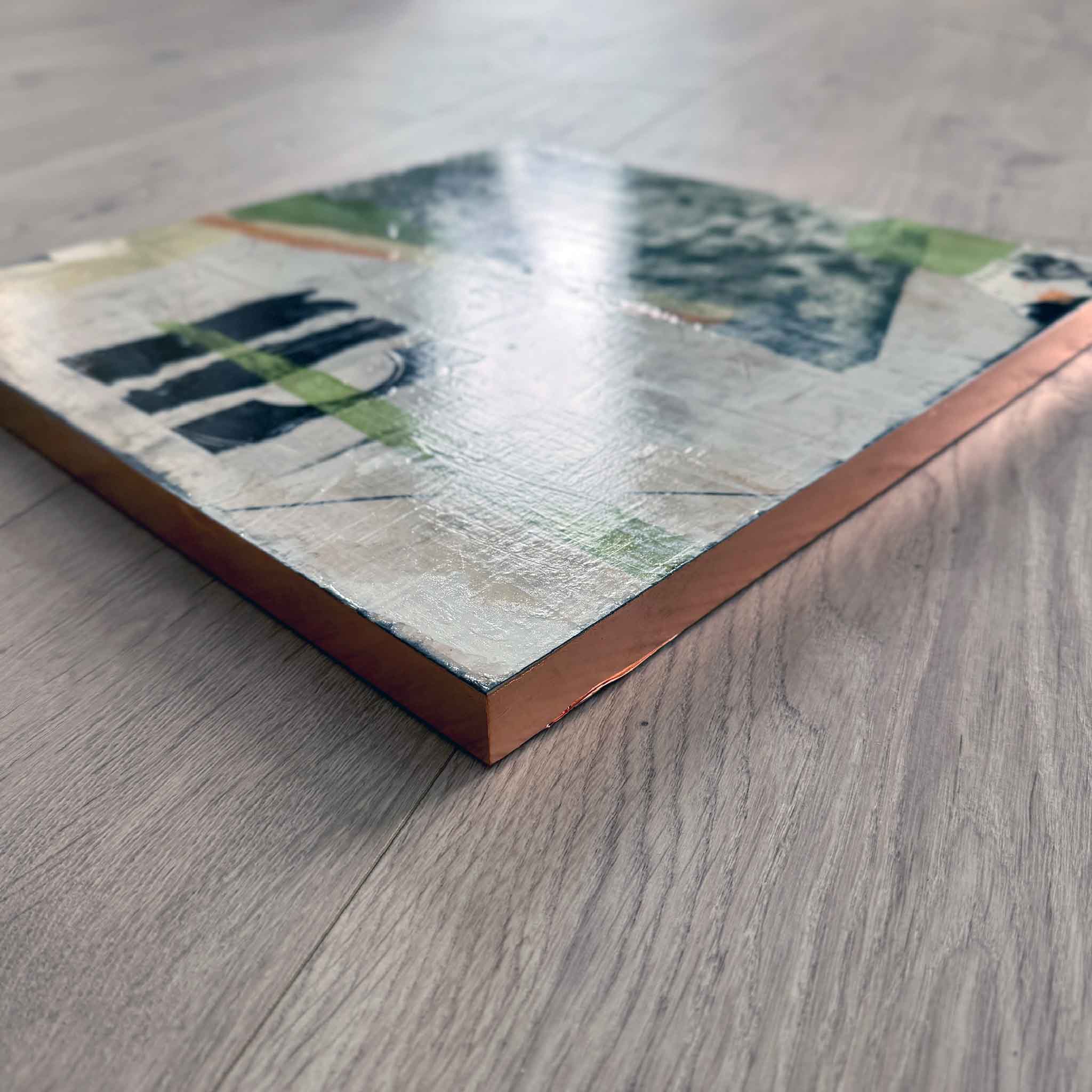 Angled view of one panel from Laurie McIntosh’s nine-piece installation, showing textured mixed-media layers and the rose-gold leafed edges catching the light.