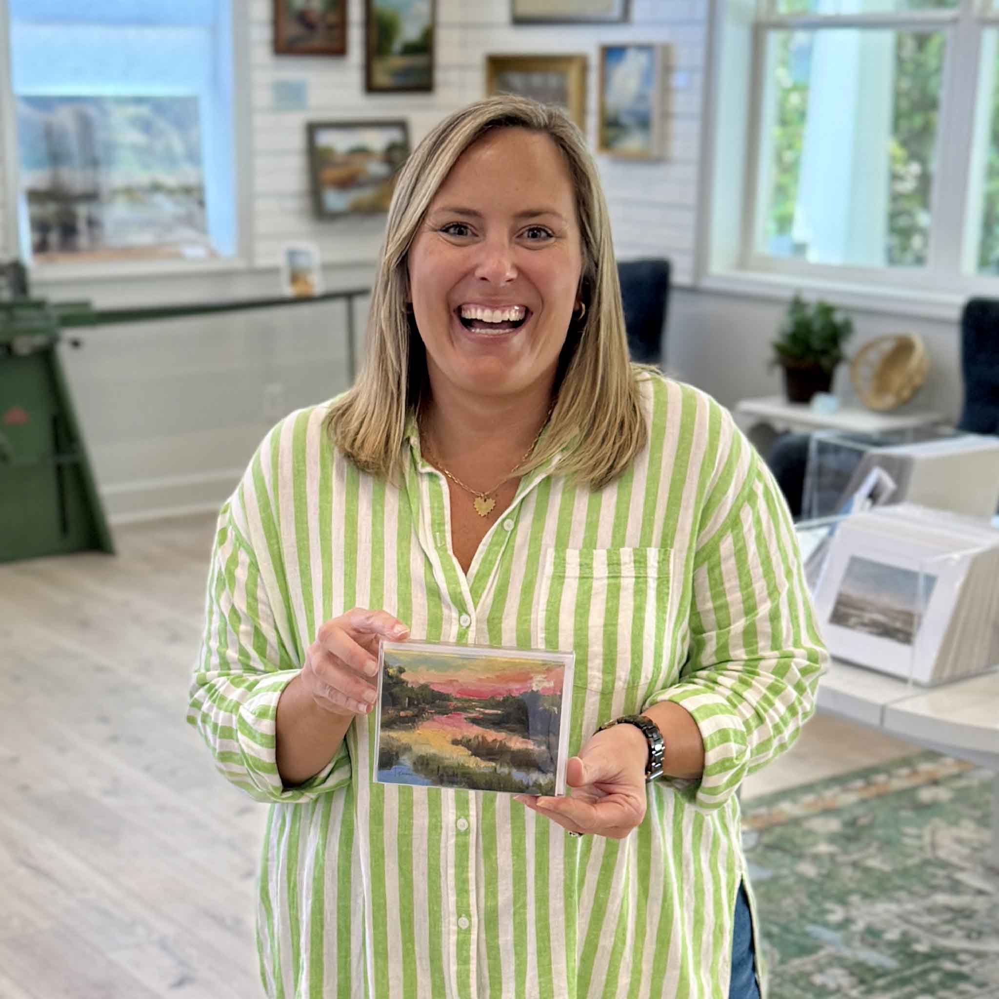 Gray Man Gallery team member holding Lowcountry Glow notecard set by local artist Jeanne O’Neal, showing size and detail of Pawleys Island marsh sunset artwork inside the gallery