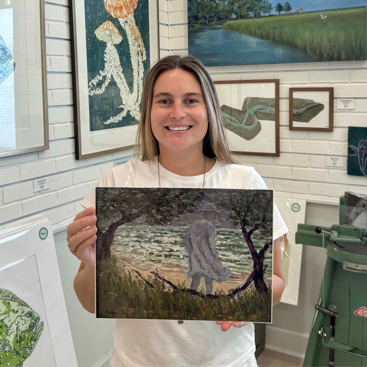 Kyra holds The Gray Man fine art giclée print by Lowcountry artist Michael Rogan at Gray Man Gallery in Pawleys Island, South Carolina, featuring Rogan’s interpretation of the legendary Gray Man walking along the windswept shoreline.