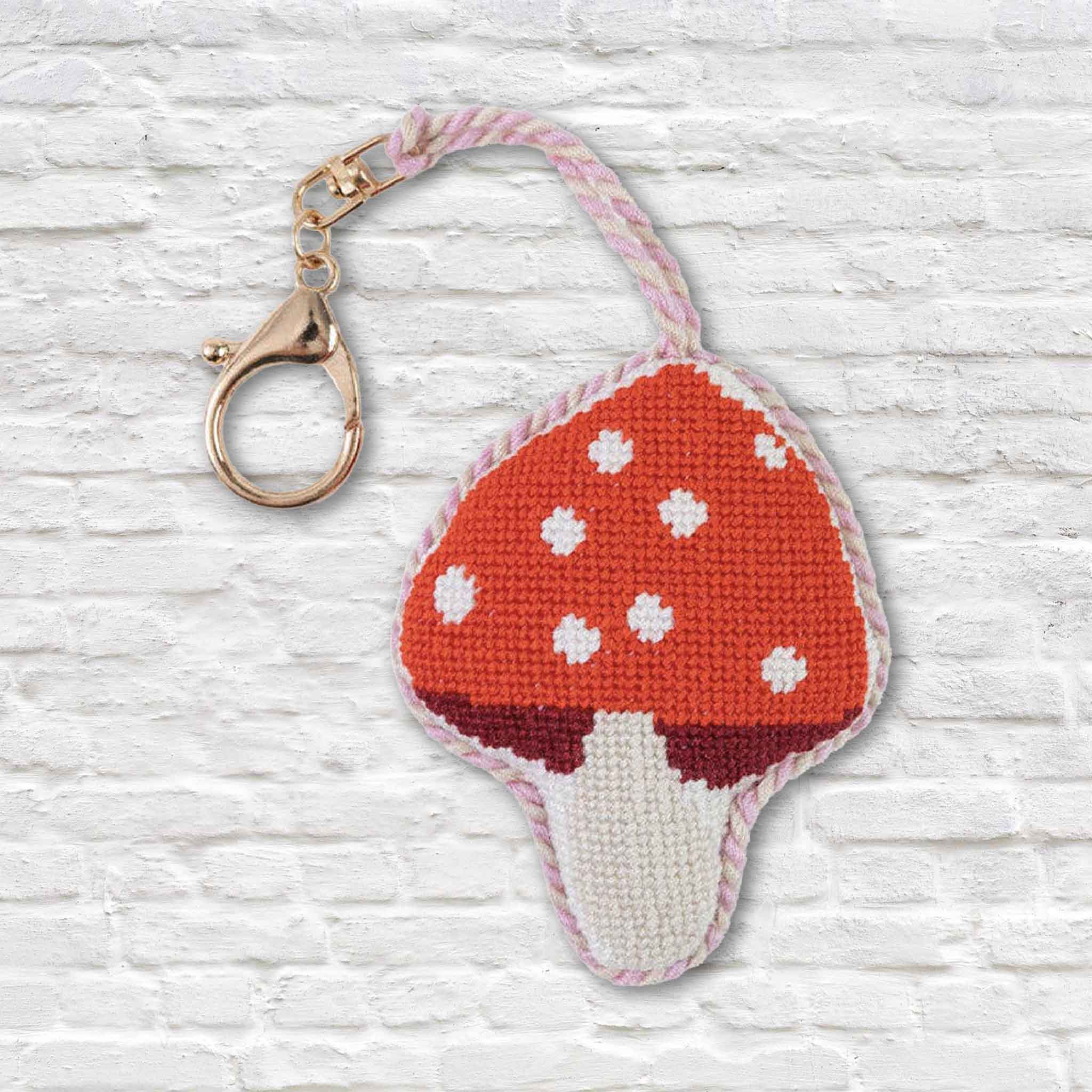 Hand-stitched mushroom needlepoint bag charm with a classic red-and-white toadstool design, soft velvet backing, pink cord, and gold-tone lobster clasp, available at Gray Man Gallery in Pawleys Island, South Carolina.