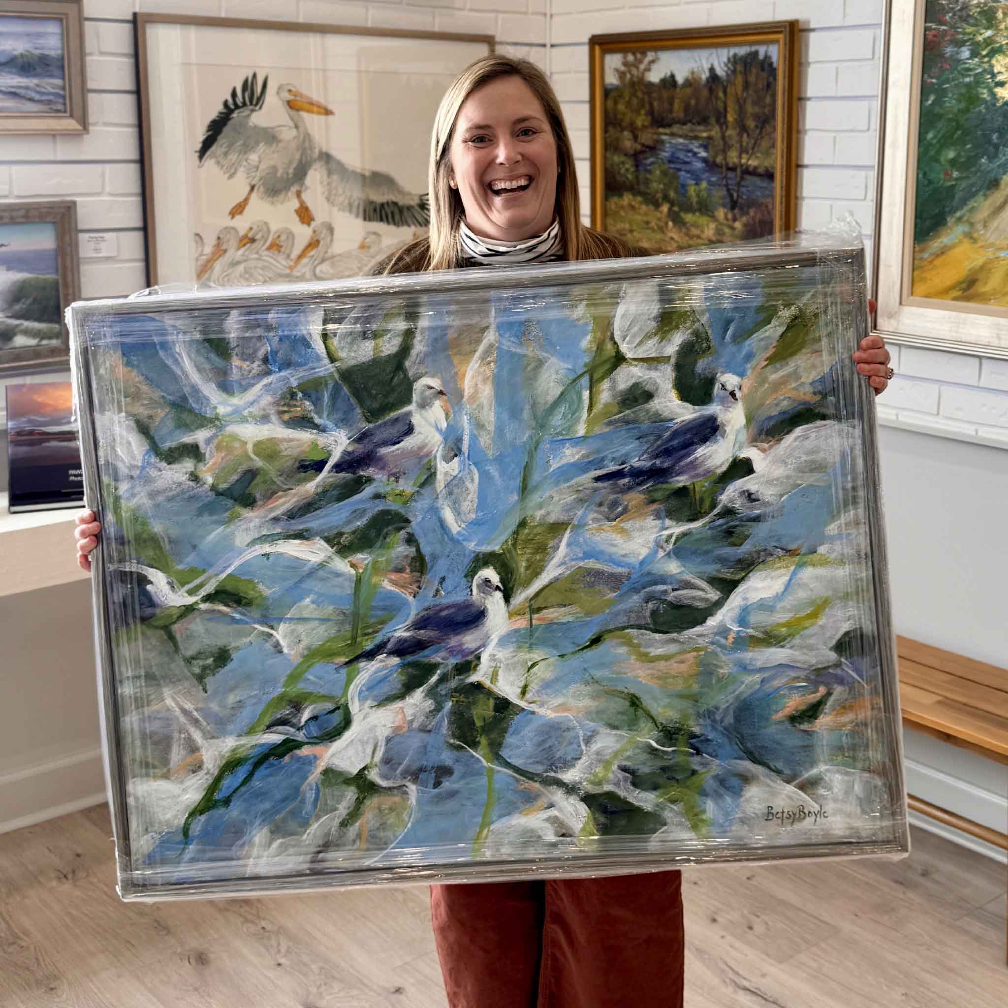 Bordy holding “Never in a Frenzy,” an original oil painting by local artist Betsy Boyle at Gray Man Gallery in Pawleys Island, featuring coastal birds in expressive Lowcountry style