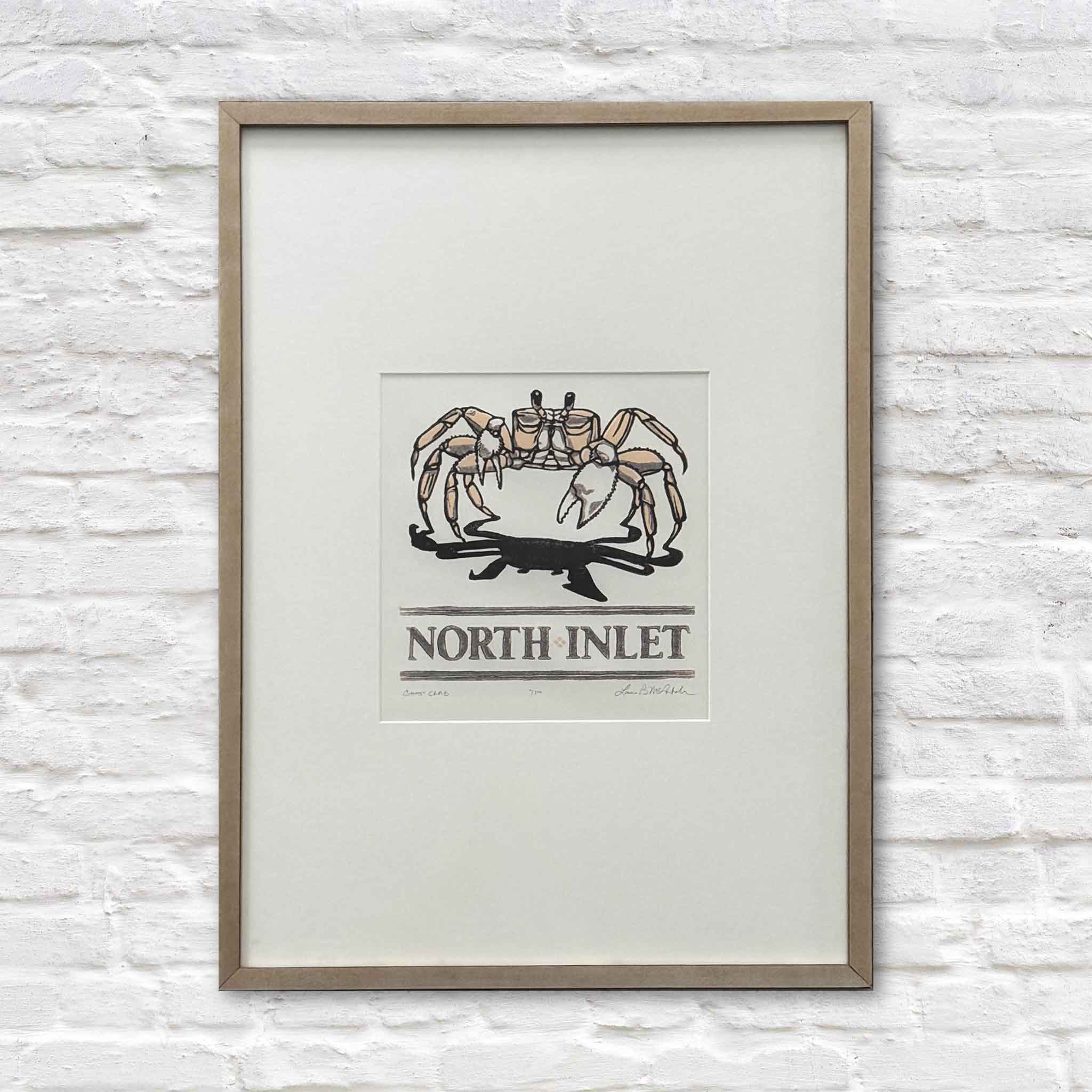North Inlet Ghost Crab framed linocut by Laurie McIntosh, custom framed with neutral mat and light wood frame, hanging on white brick wall at Gray Man Gallery Pawleys Island.