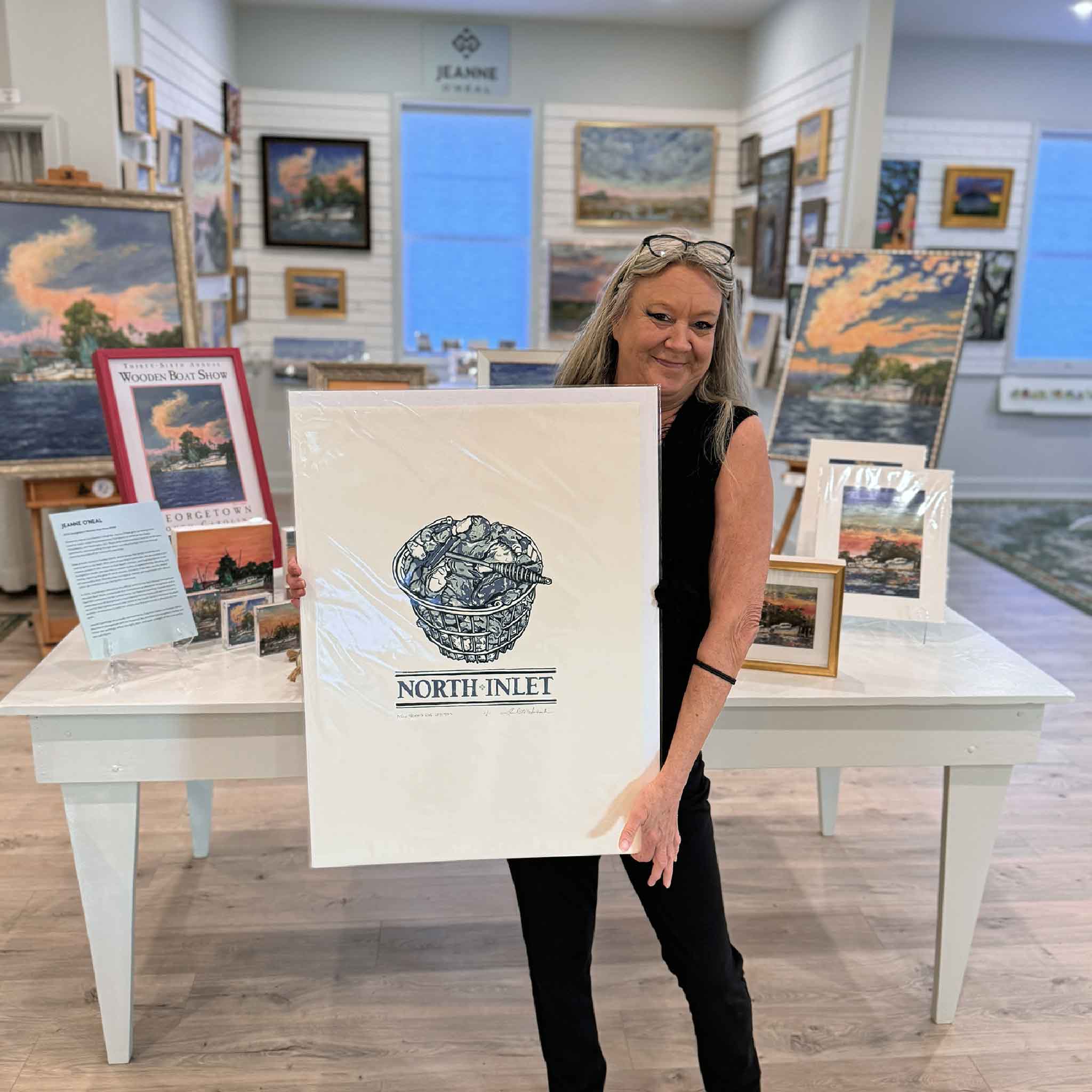 Charlotte holding the blue North Inlet oyster linocut print by Laurie McIntosh at Gray Man Gallery.