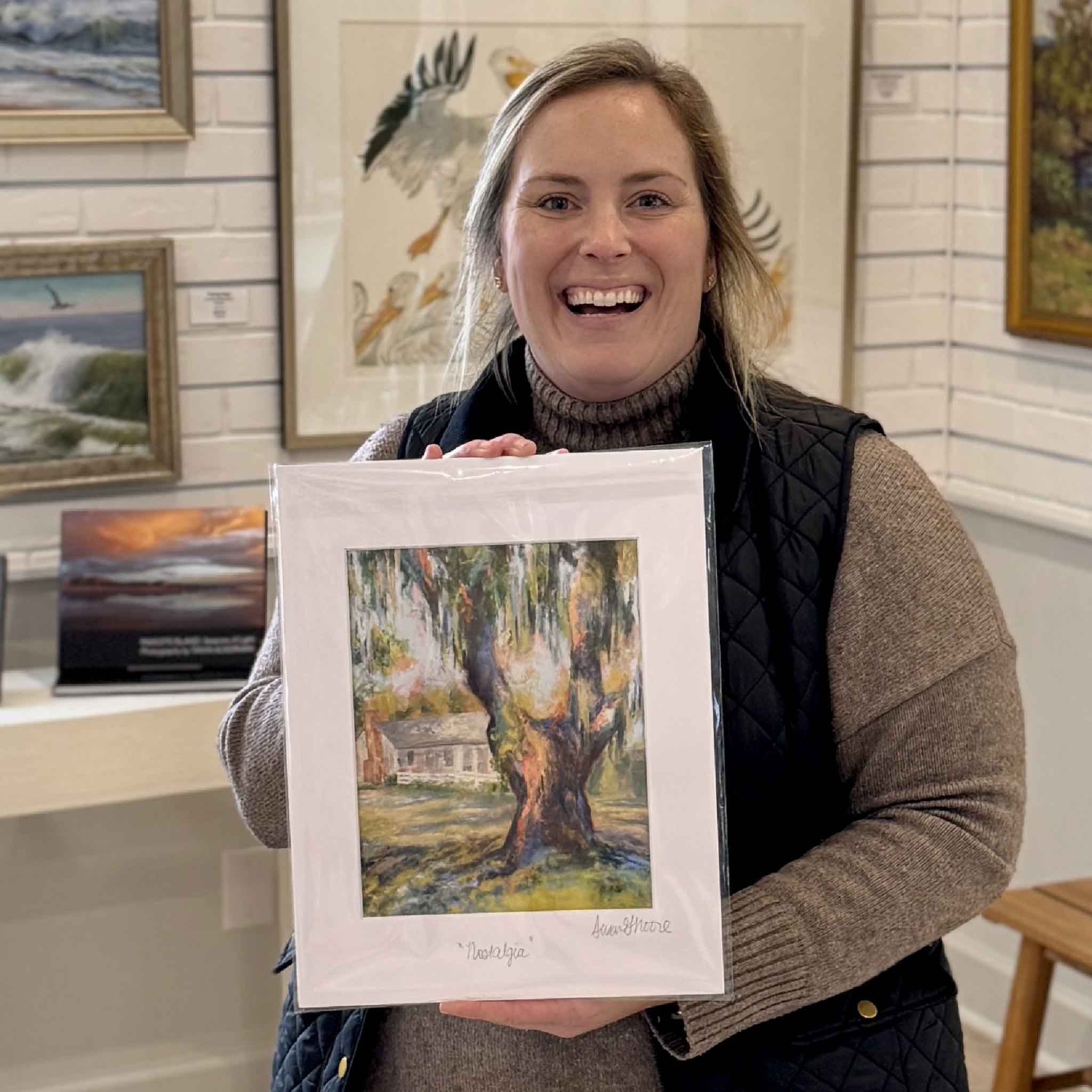 Bordy holding signed Nostalgia fine art giclée print by local artist Susan Moore inside Gray Man Gallery in Pawleys Island, featuring Southern cottage and oak tree landscape, matted 11x14 artwork on display