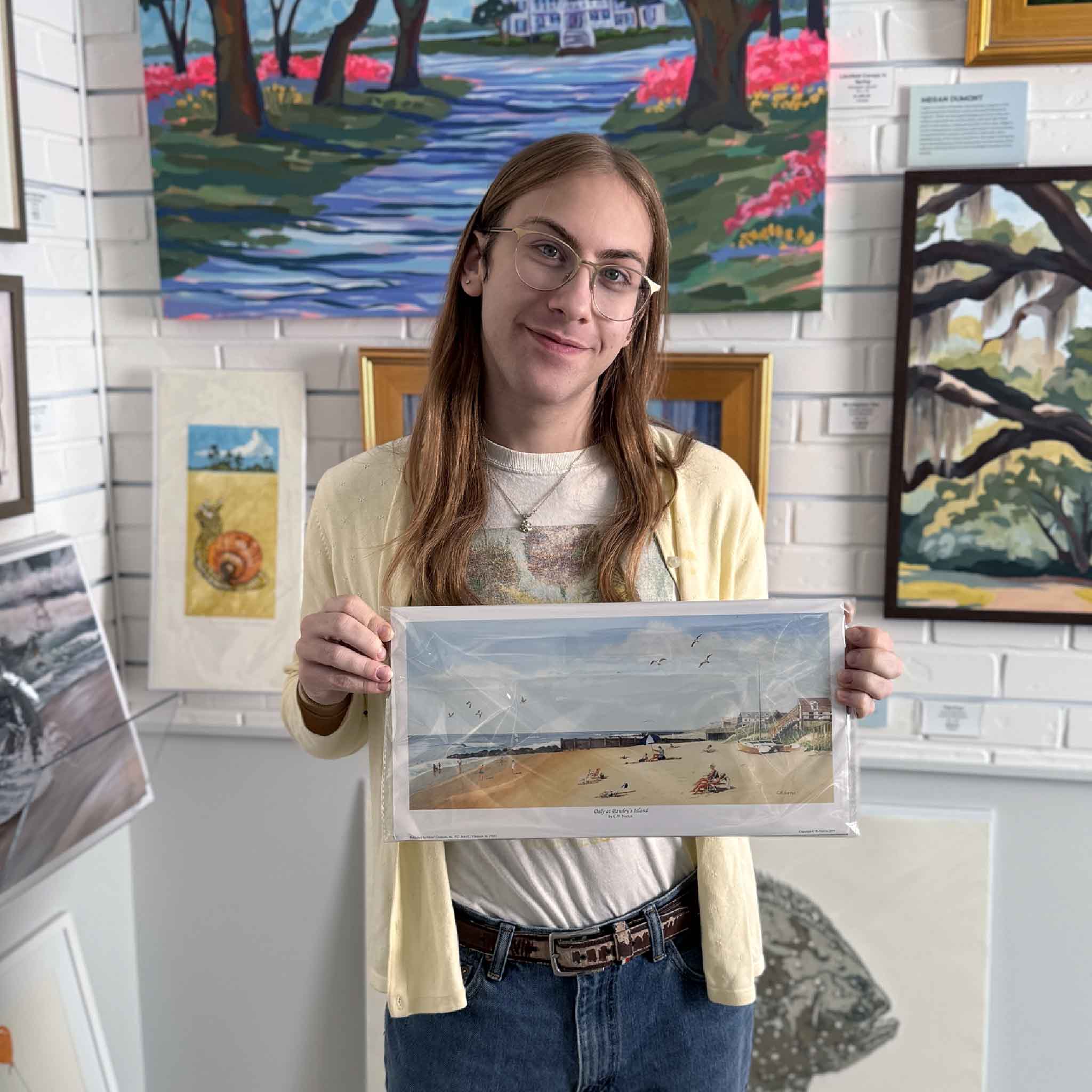 A person holds the C.W. Norton Pawleys Island beach print inside Gray Man Gallery, showing the scale and detail of the artwork.