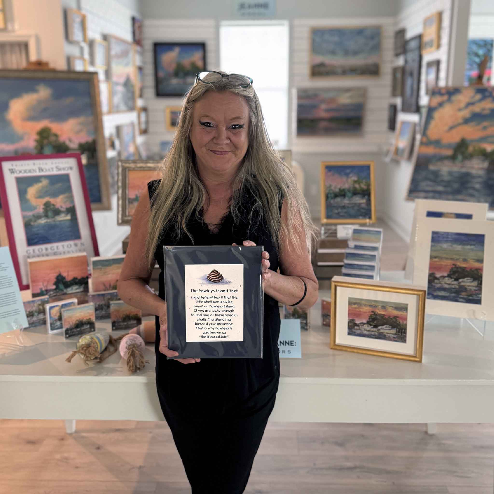 Charlotte holding the matted Pawleys Island Shell Legend print by Vida Miller inside Gray Man Gallery, highlighting the standard 8x10 mat size and the artwork’s role as a cherished Pawleys Island gift and coastal folklore keepsake.