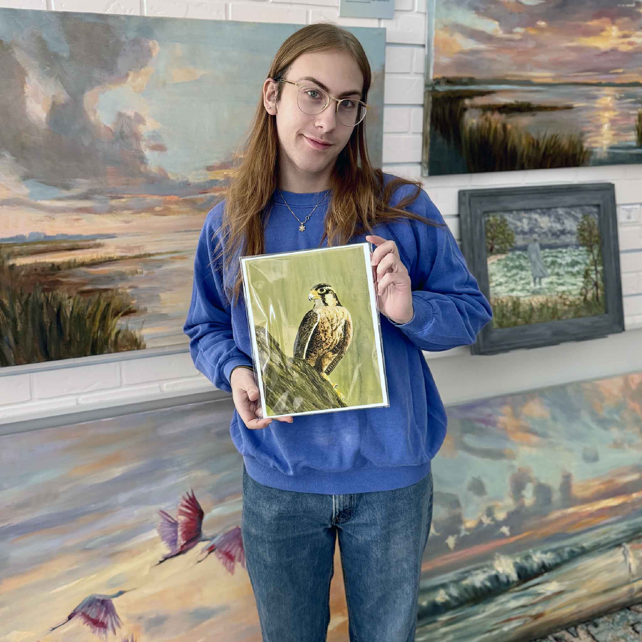 A Gray Man Gallery team member holds Peregrine Watch by Mimi Beaver, a raptor artwork offered as a charitable donation piece with 100 percent of proceeds benefiting Salty Dogs Senior Animal Rescue.