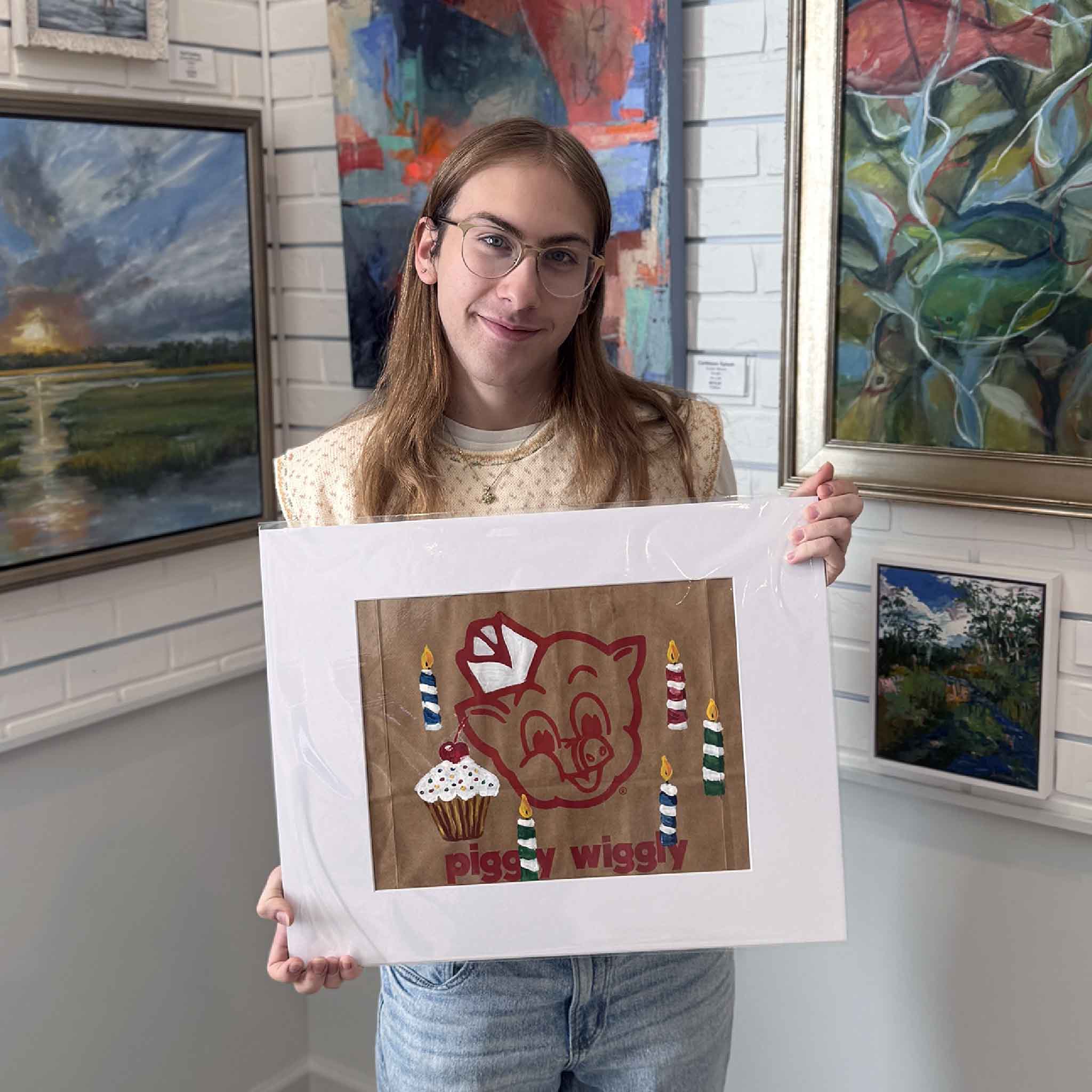 Gray Man Gallery team member holding the matted “Happy Birthday” Piggly Wiggly artwork to show size and scale.