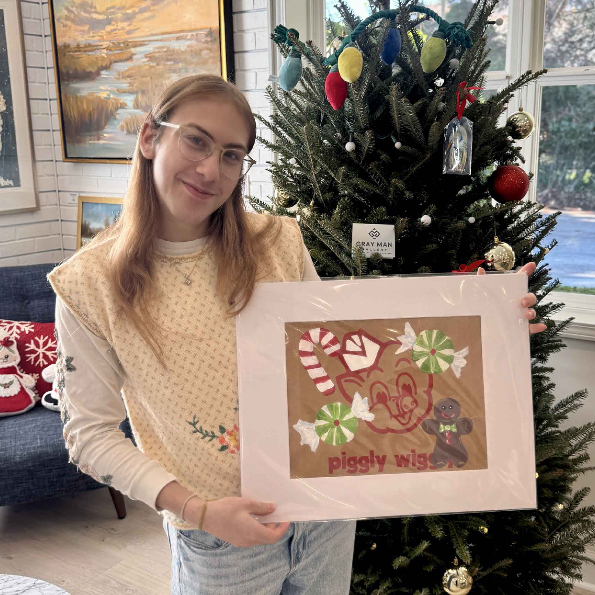 A Gray Man Gallery team member holding the Piggly Wiggly Holiday Treats original by Jenny Reynolds, showing its scale and festive Christmas details.