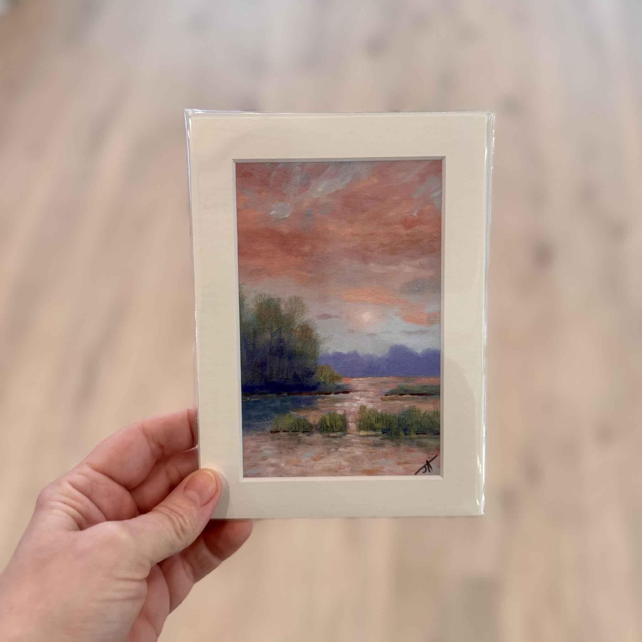 Quiet After the Storm, held for scale inside Gray Man Gallery, is a small fine art print by Jamie Arnold, depicting a peaceful Lowcountry marsh at dusk with soft pastel skies, matted to 5x7 to fit a standard frame.