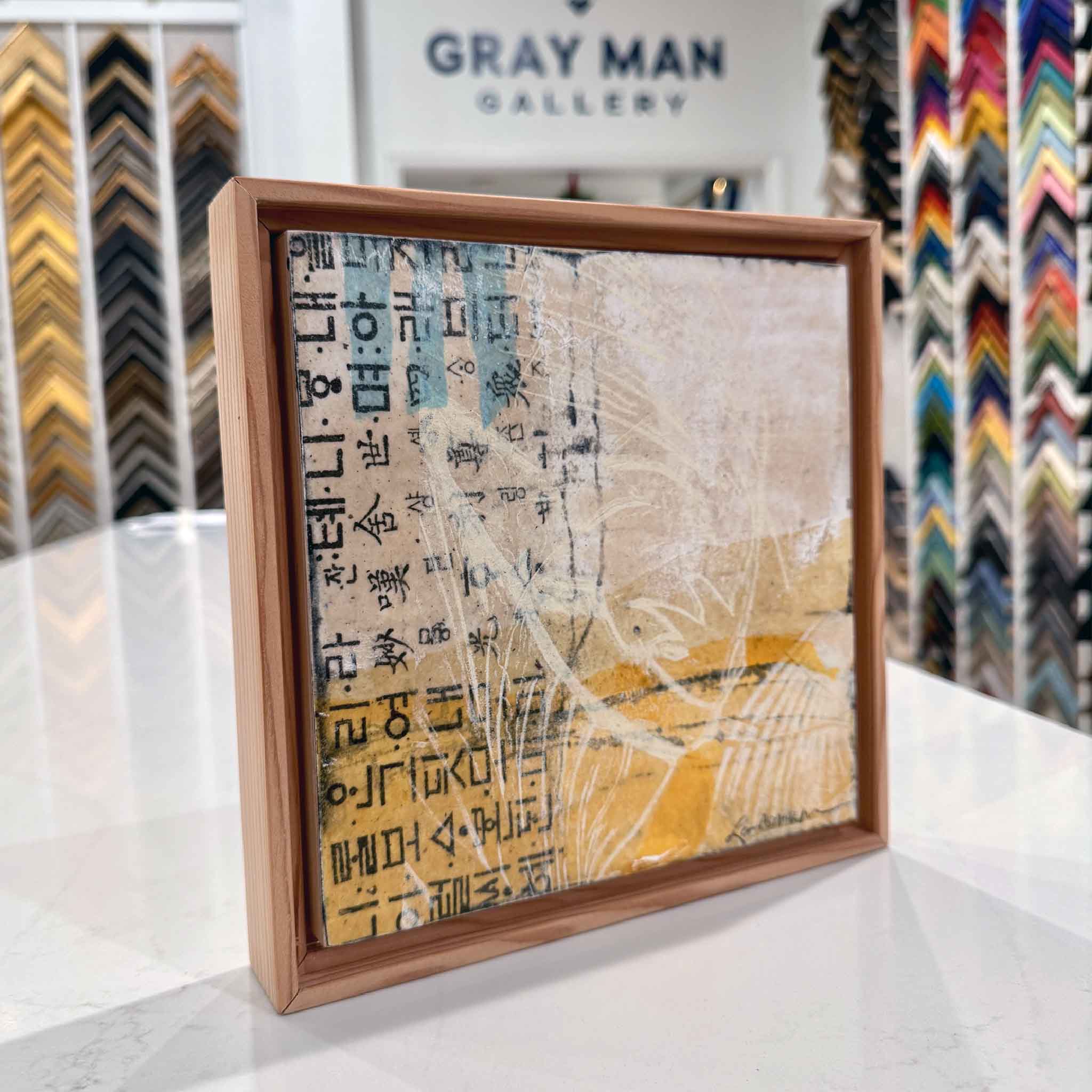 Side-angle view of the Residuals 5D mixed-media artwork showing the textured surface, layered collage elements, and the natural wood floater frame displayed inside Gray Man Gallery.