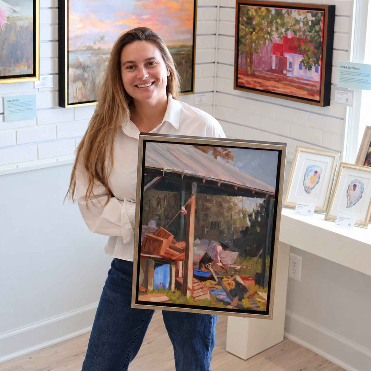 Gray Man Gallery team member holding Oyster Shoveler #220, an original oil painting by local artist Retta Dotterer depicting a South Carolina oyster worker, shown for scale inside Gray Man Gallery in Pawleys Island.
