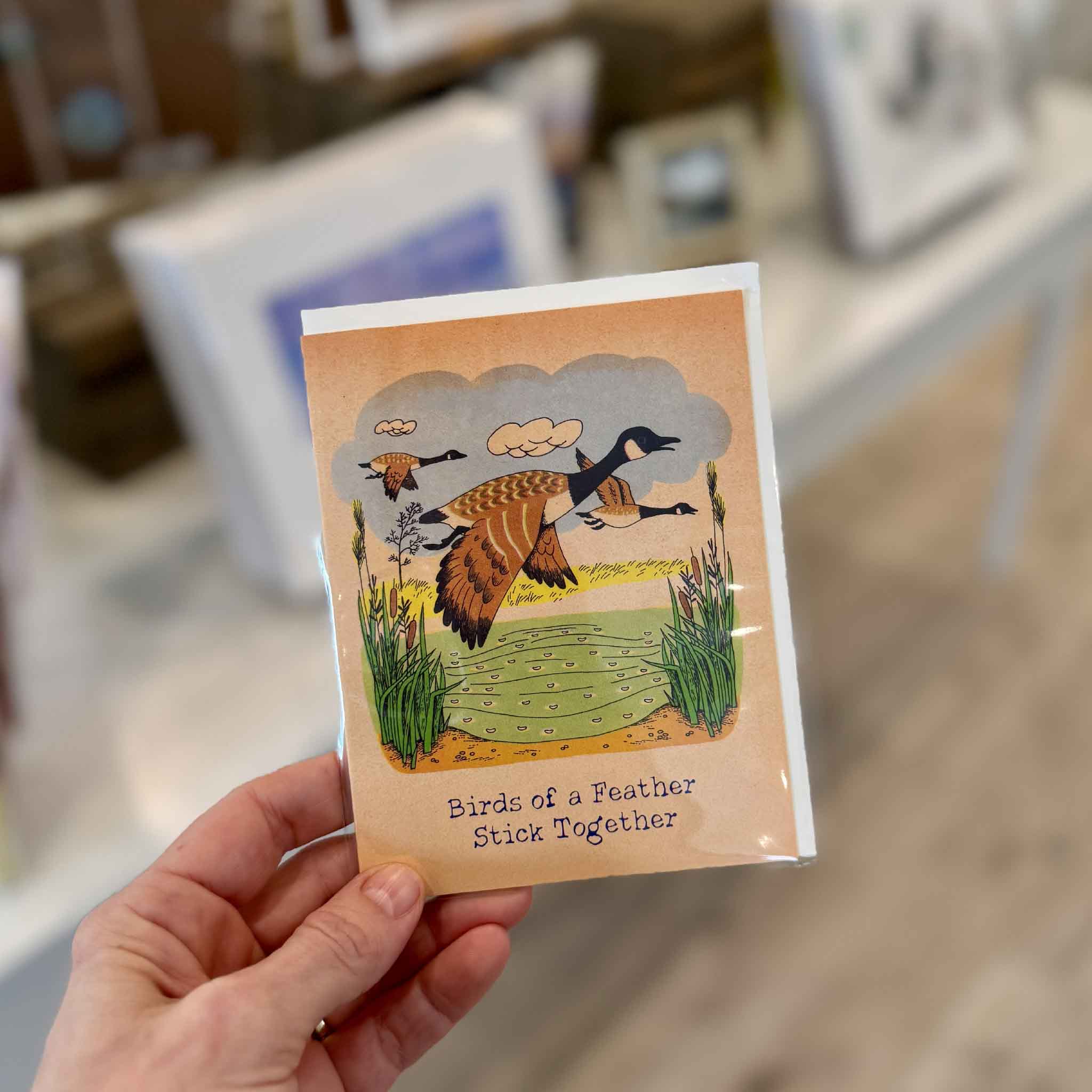 Richard Scarry Birds of a Feather greeting card held inside Gray Man Gallery in Pawleys Island, featuring nostalgic geese artwork and the message “Birds of a Feather Stick Together.”