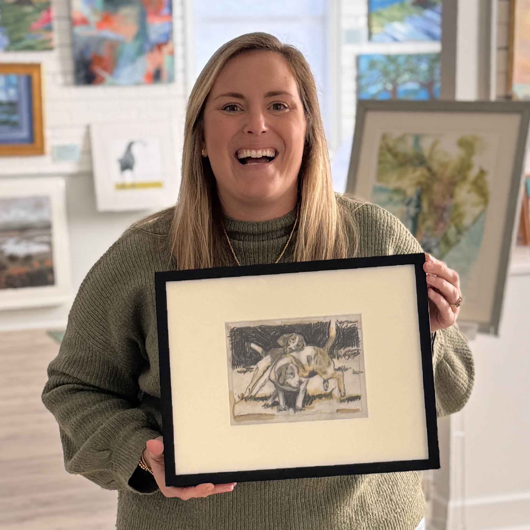 Gallery team member holding Roughhousing by local artist Laurie McIntosh to show scale, a one-of-a-kind original monoprint featuring playful dogs, photographed inside Gray Man Gallery.