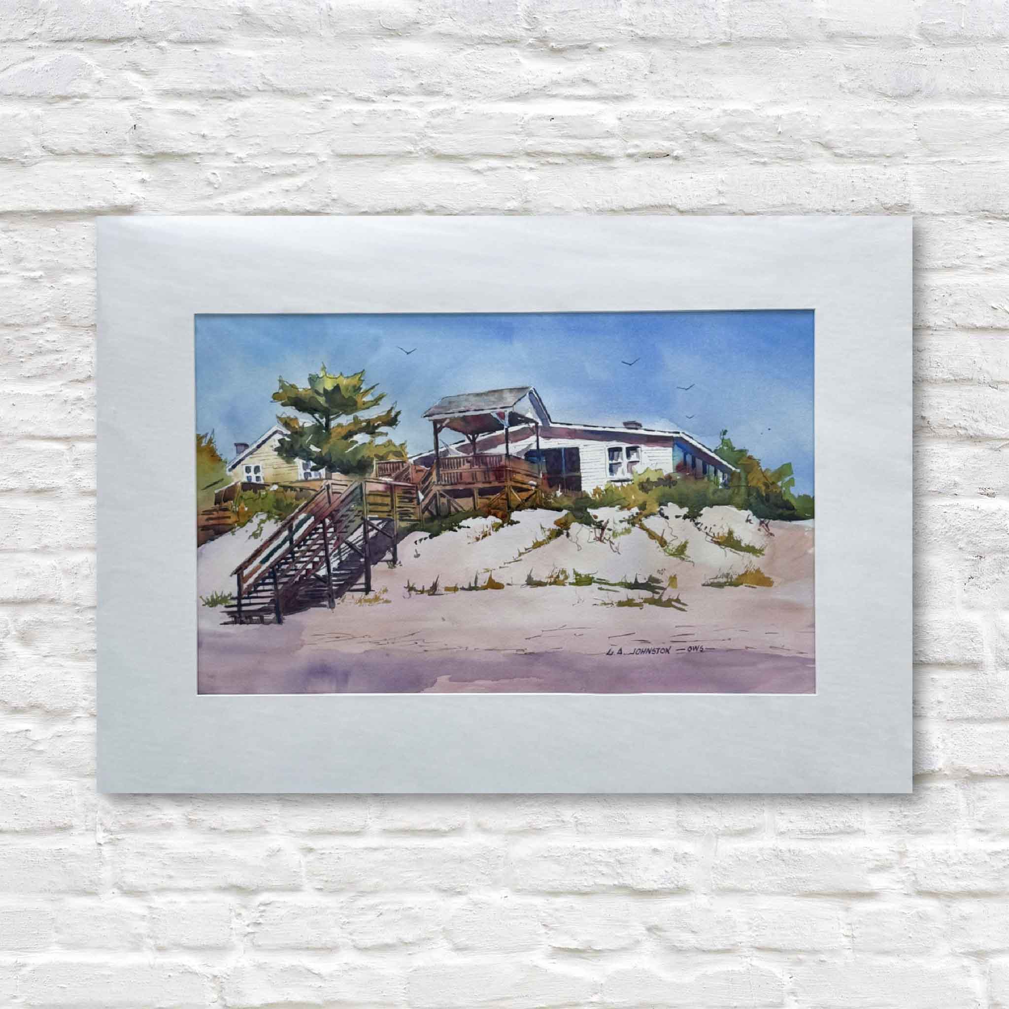 A matted watercolor painting by Gary Johnston depicting a classic Pawleys Island beach house with sandy dunes, wooden walkways, and a bright coastal sky.