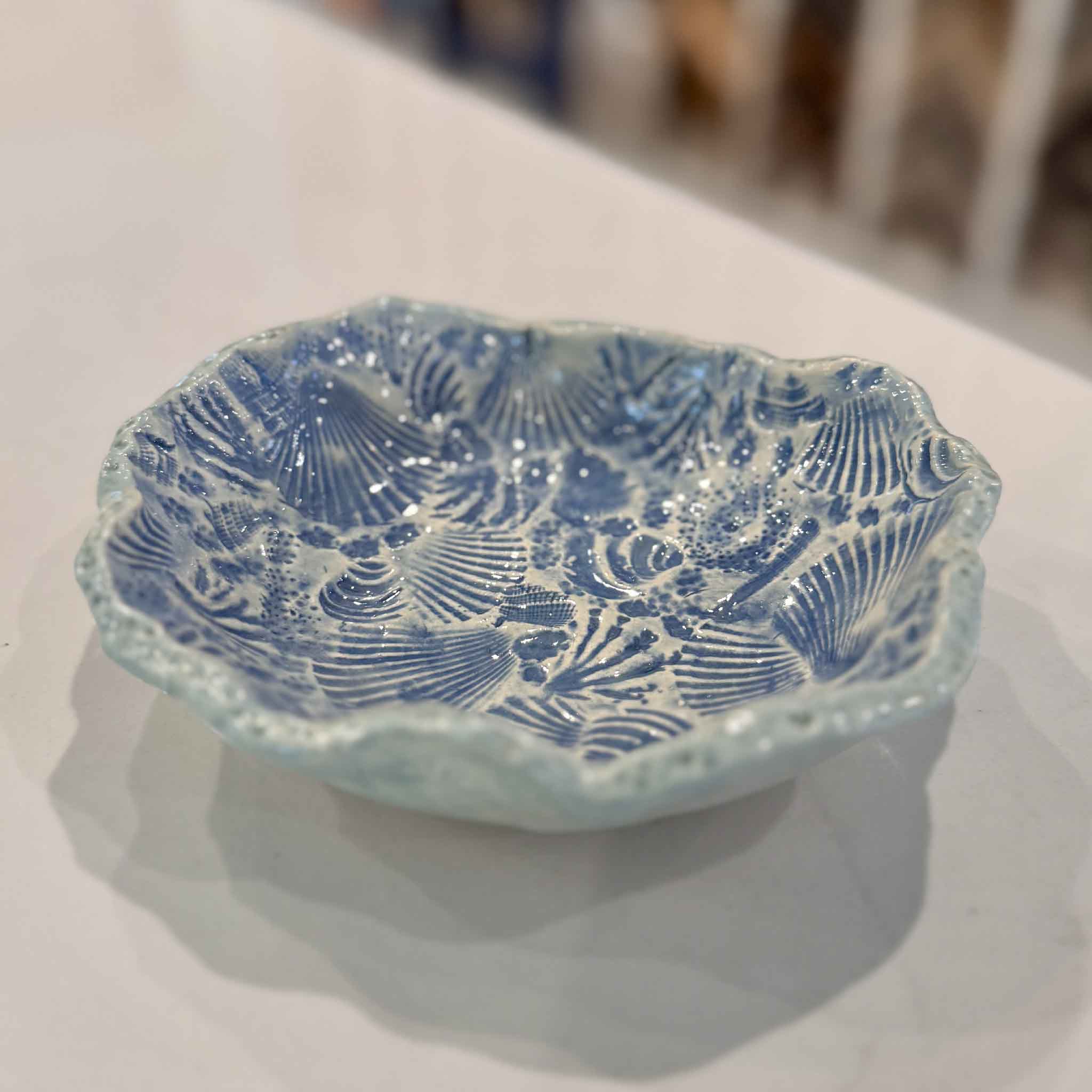 Close angled view of Pawleys Shore Shell Dish in Sea Glass Blue by local artist Vida Miller highlighting layered shell impressions and glossy blue glaze