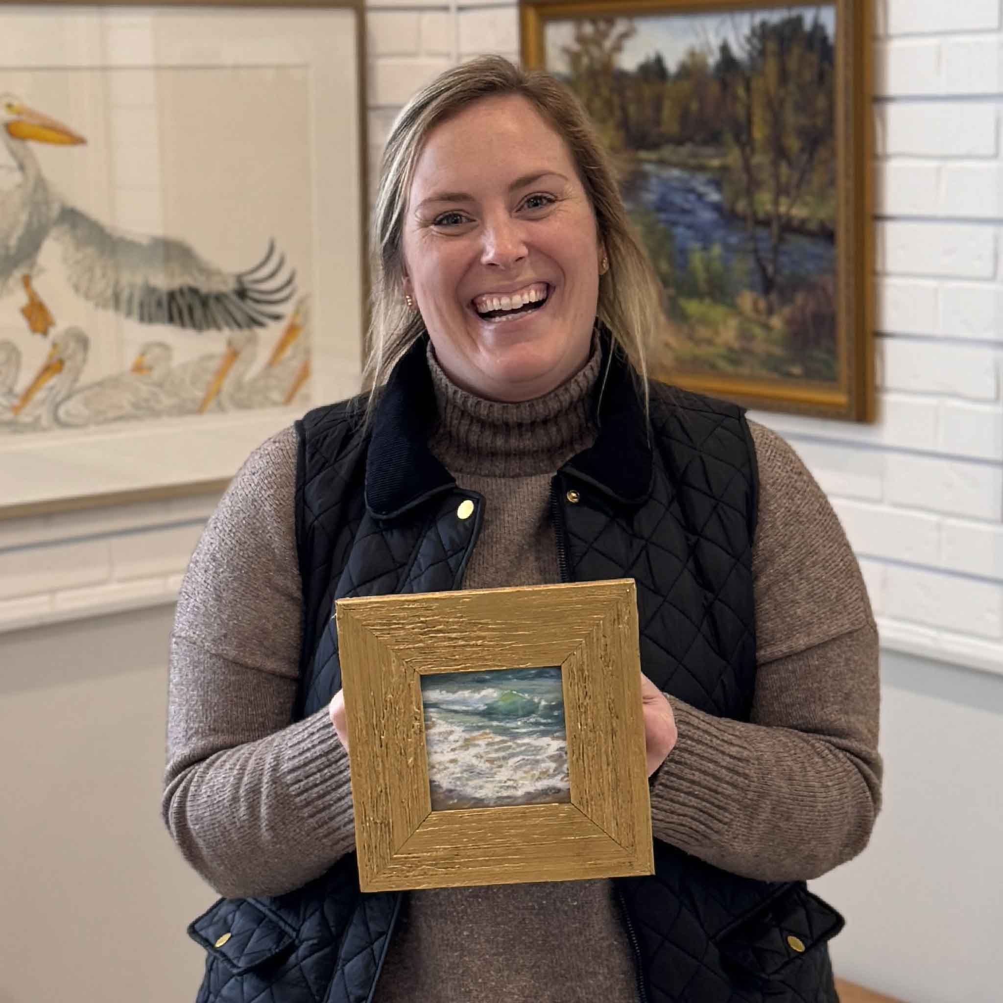 Bordy at Gray Man Gallery in Pawleys Island, South Carolina holding “Sparkle,” a small original pastel artwork by local Lowcountry artist Joanne Willoughby, professionally framed in textured gold molding, featuring a peaceful coastal shoreline scene with soft blues, seafoam greens, and white highlights, showcasing custom framing craftsmanship, local art, and boutique gallery atmosphere