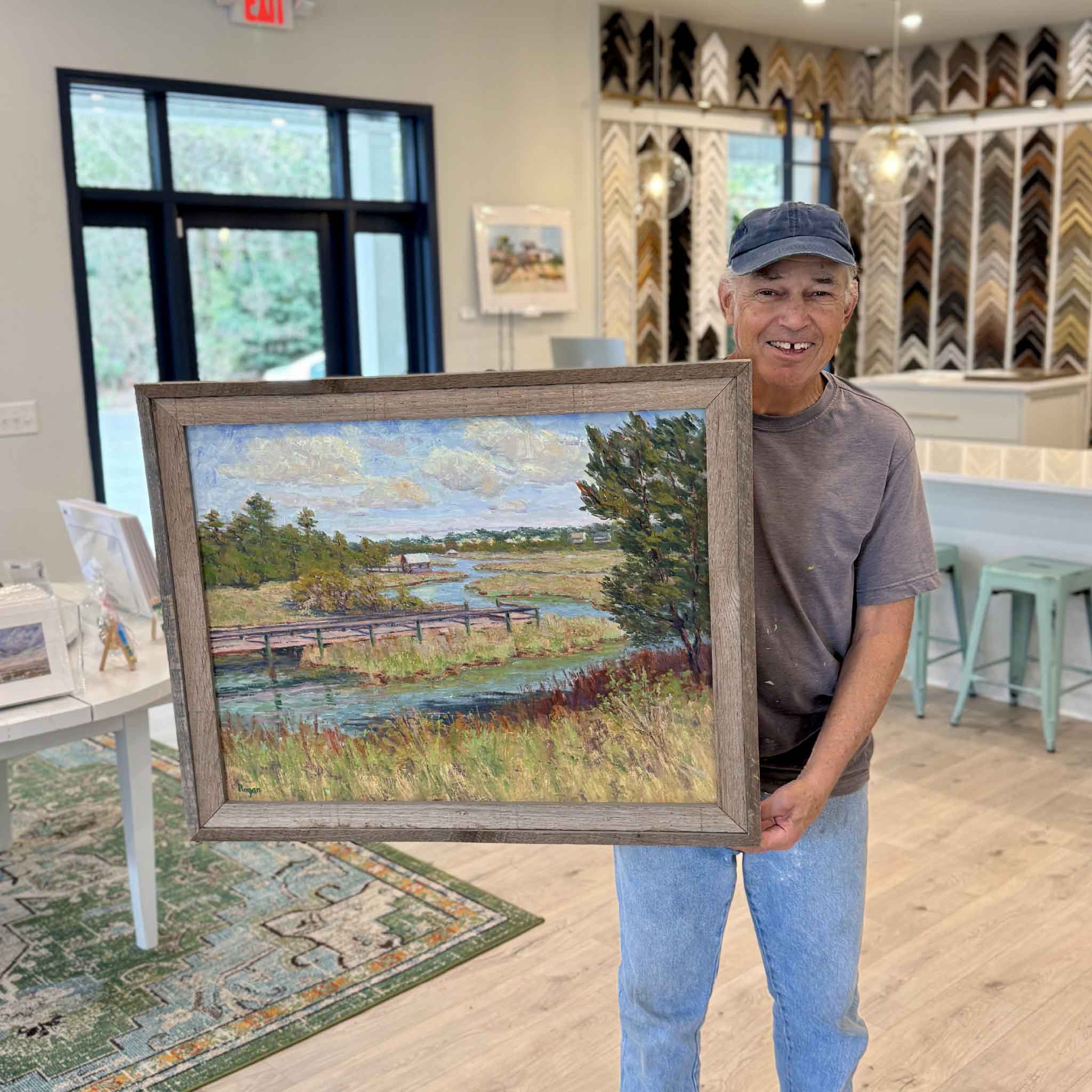 Local artist Michael Rogan holding his Spring Creek South Litchfield marsh oil painting at Gray Man Gallery in Pawleys Island South Carolina