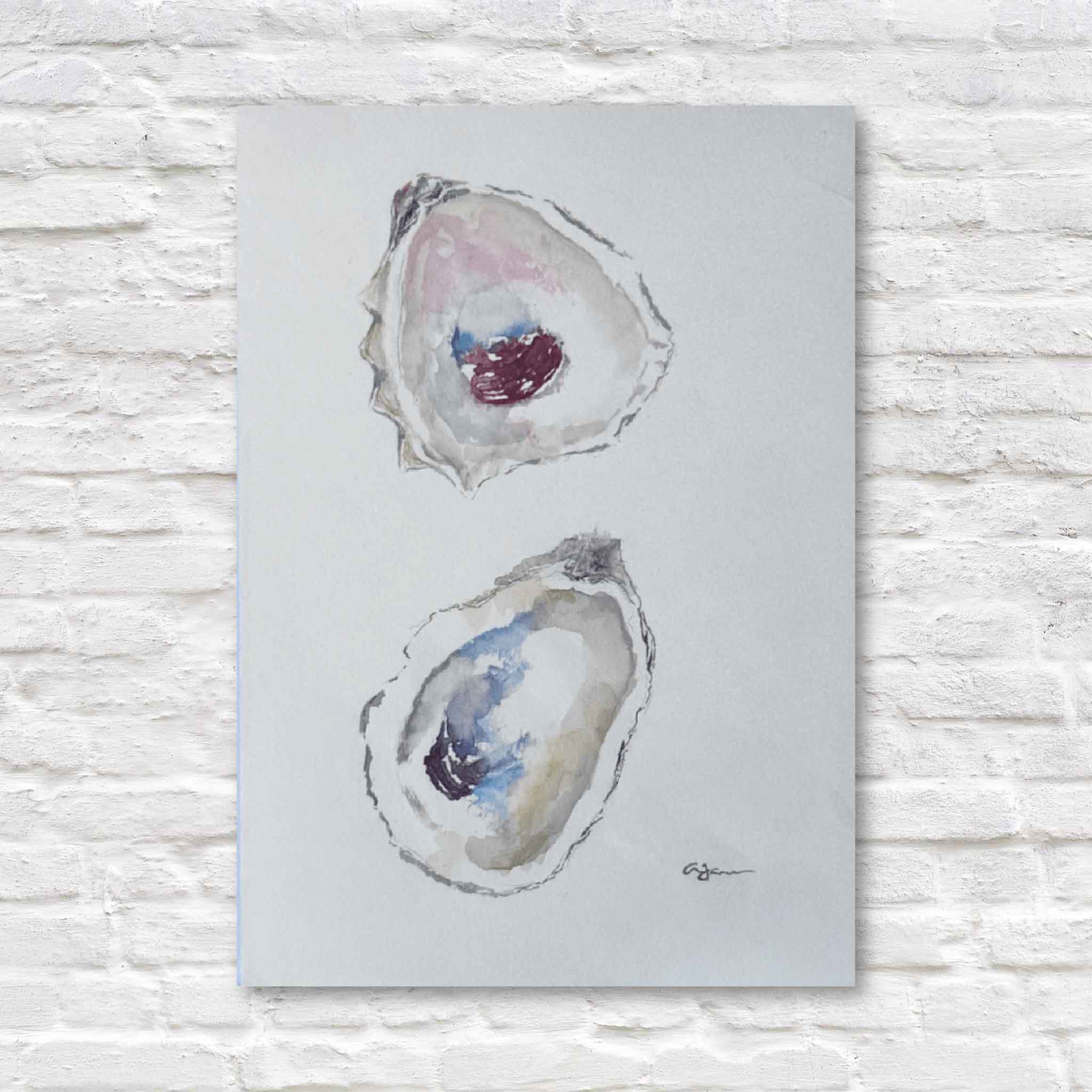 Original watercolor oyster painting titled Stillness by local Lowcountry artist Allison Farr, featuring two hand-painted oyster shells in soft coastal blues, blush, and gray, photographed at Gray Man Gallery in Pawleys Island, South Carolina