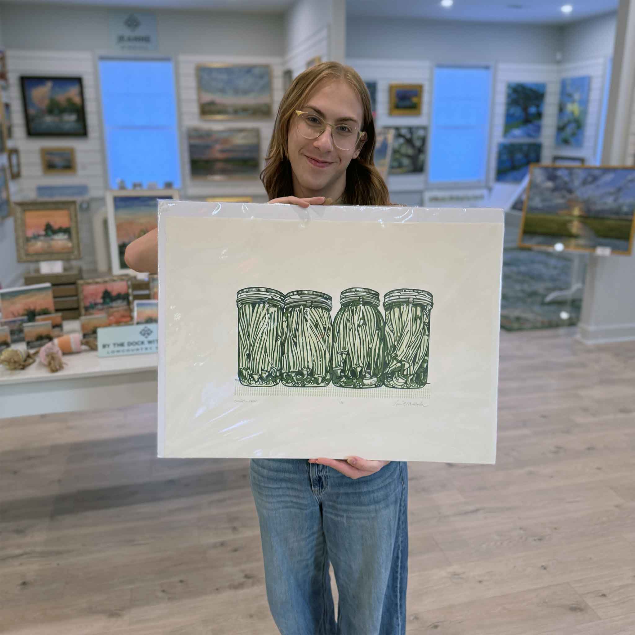 Alex holding ‘Summer Okra,’ an original green okra jar linocut by artist Laurie McIntosh at Gray Man Gallery”