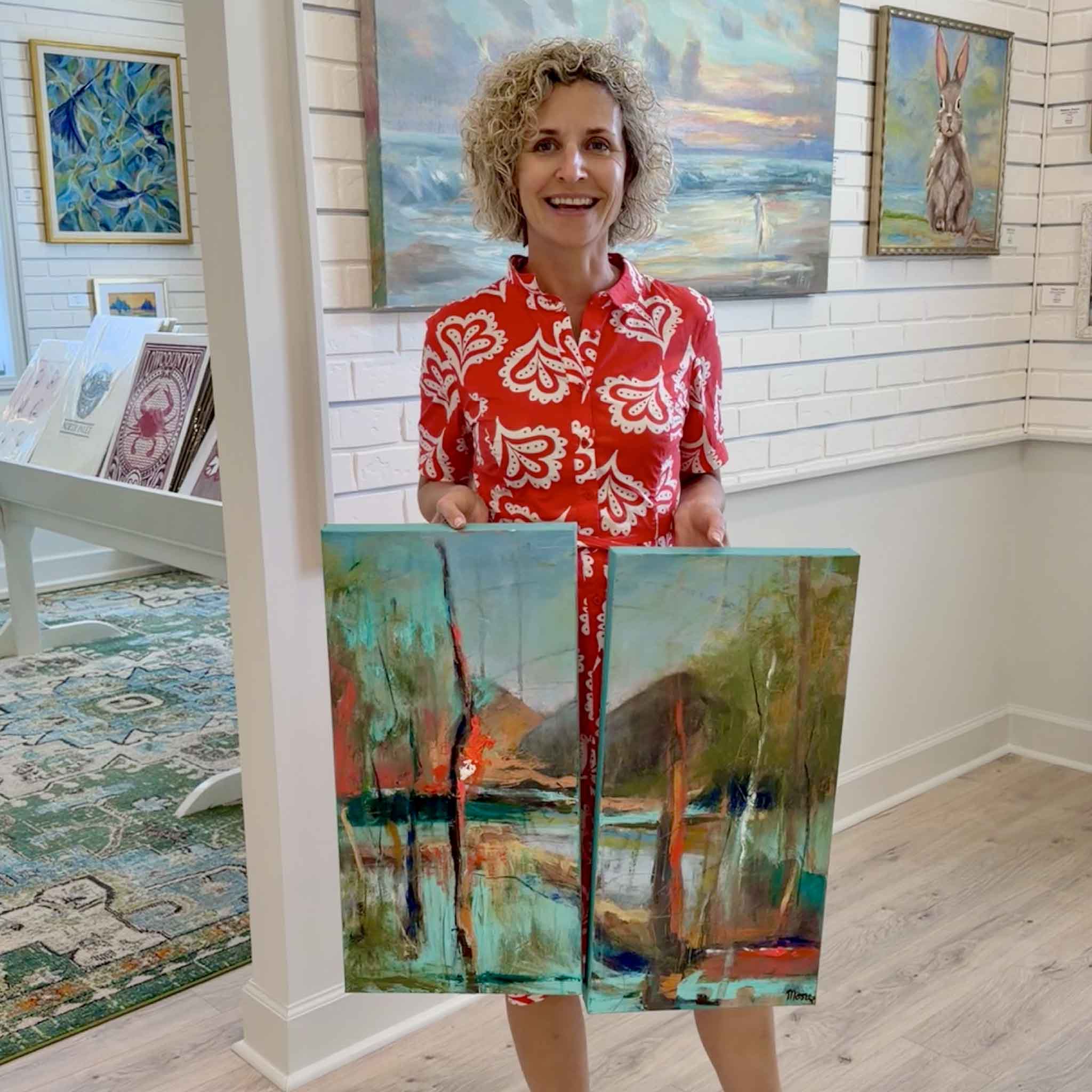 Susan Moore holding Summer Cypress diptych inside Gray Man Gallery Pawleys Island showing scale of two 12x24 abstract acrylic paintings with layered coastal colors and vertical tree-like forms