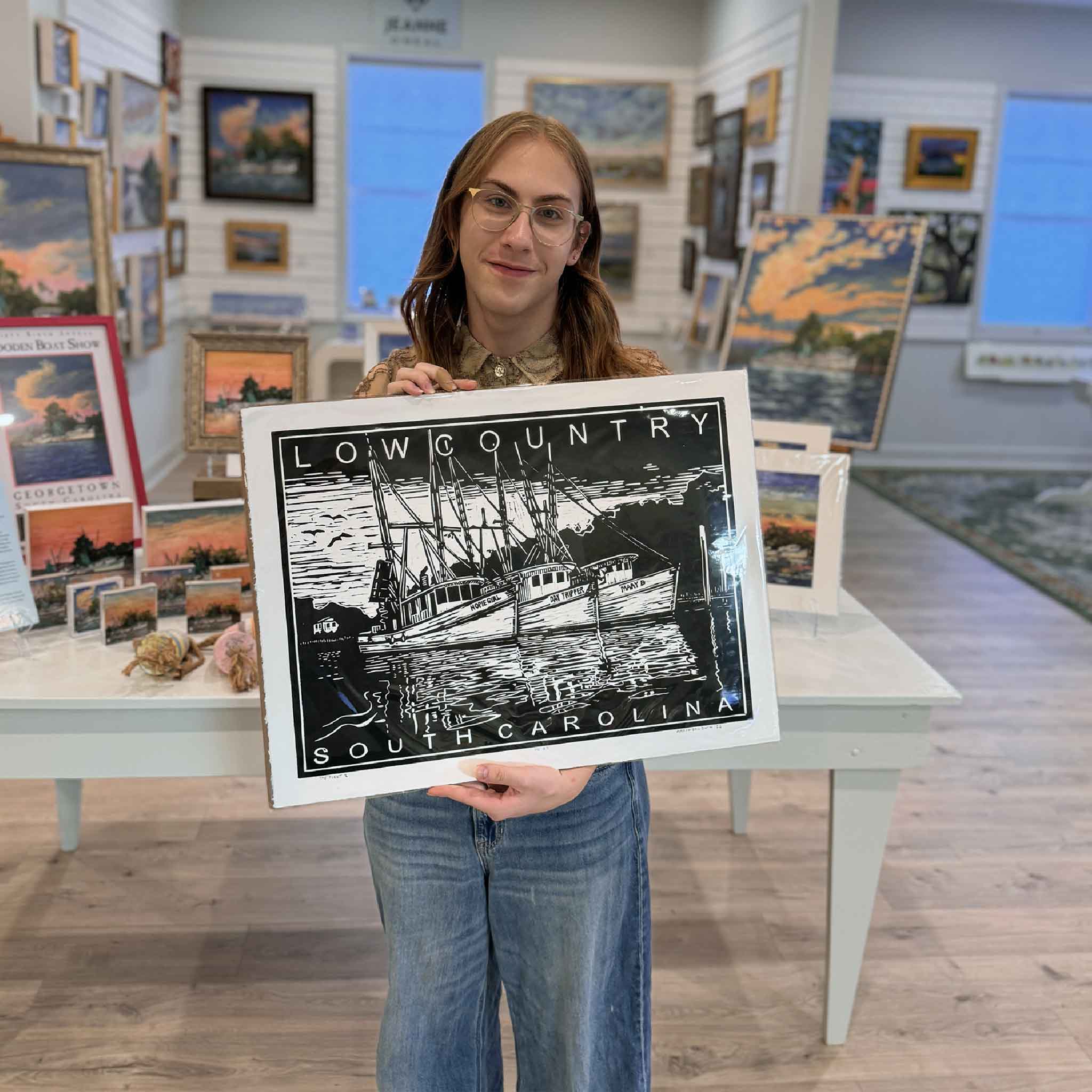 Alex holding The Fleet II linocut print in black by Aaron Baldwin inside Gray Man Gallery.