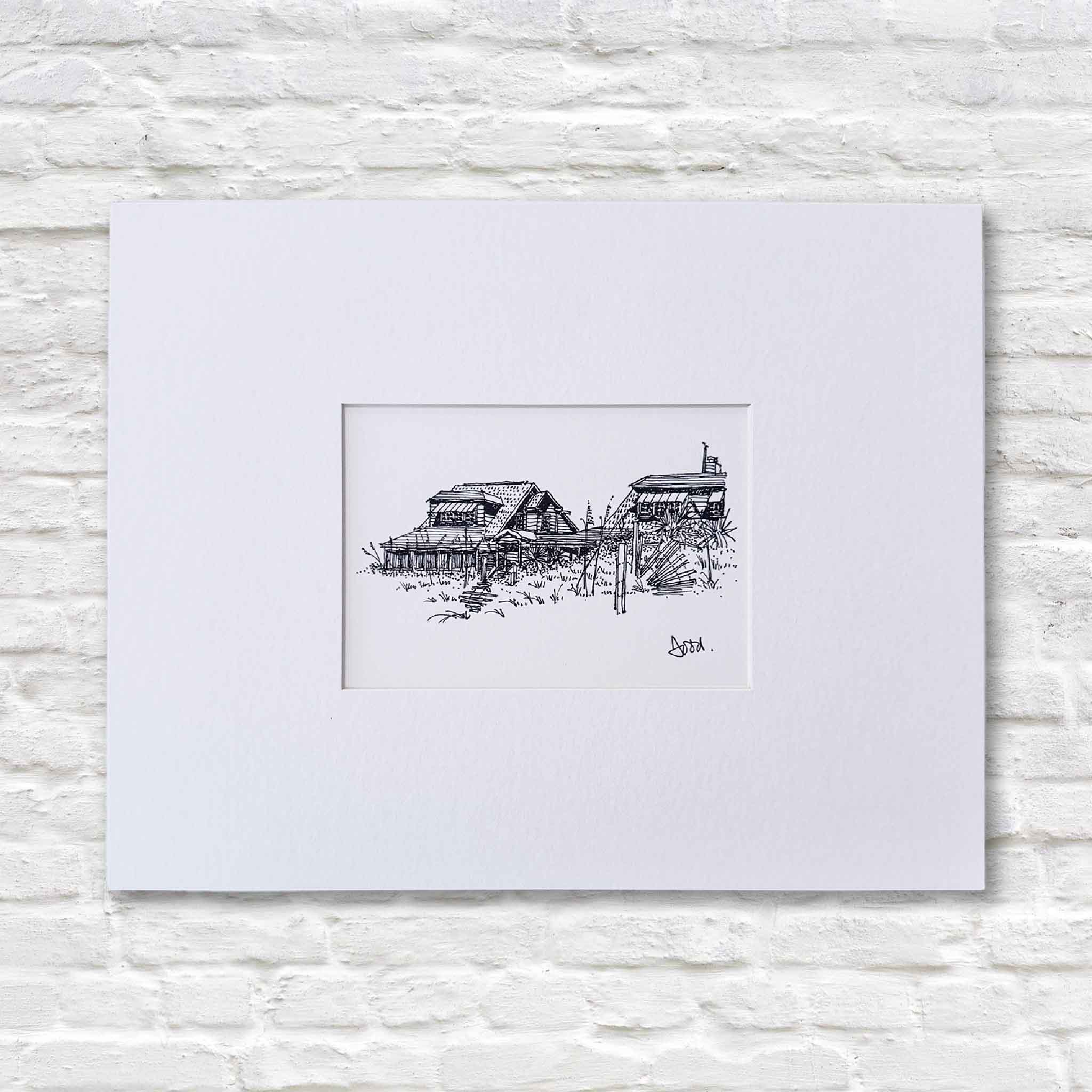 Matted 14x11 pen-and-ink coastal print by Lowcountry artist Todd Halamka, featuring two Pawleys Island beach cottages against a white brick wall in Gray Man Gallery.