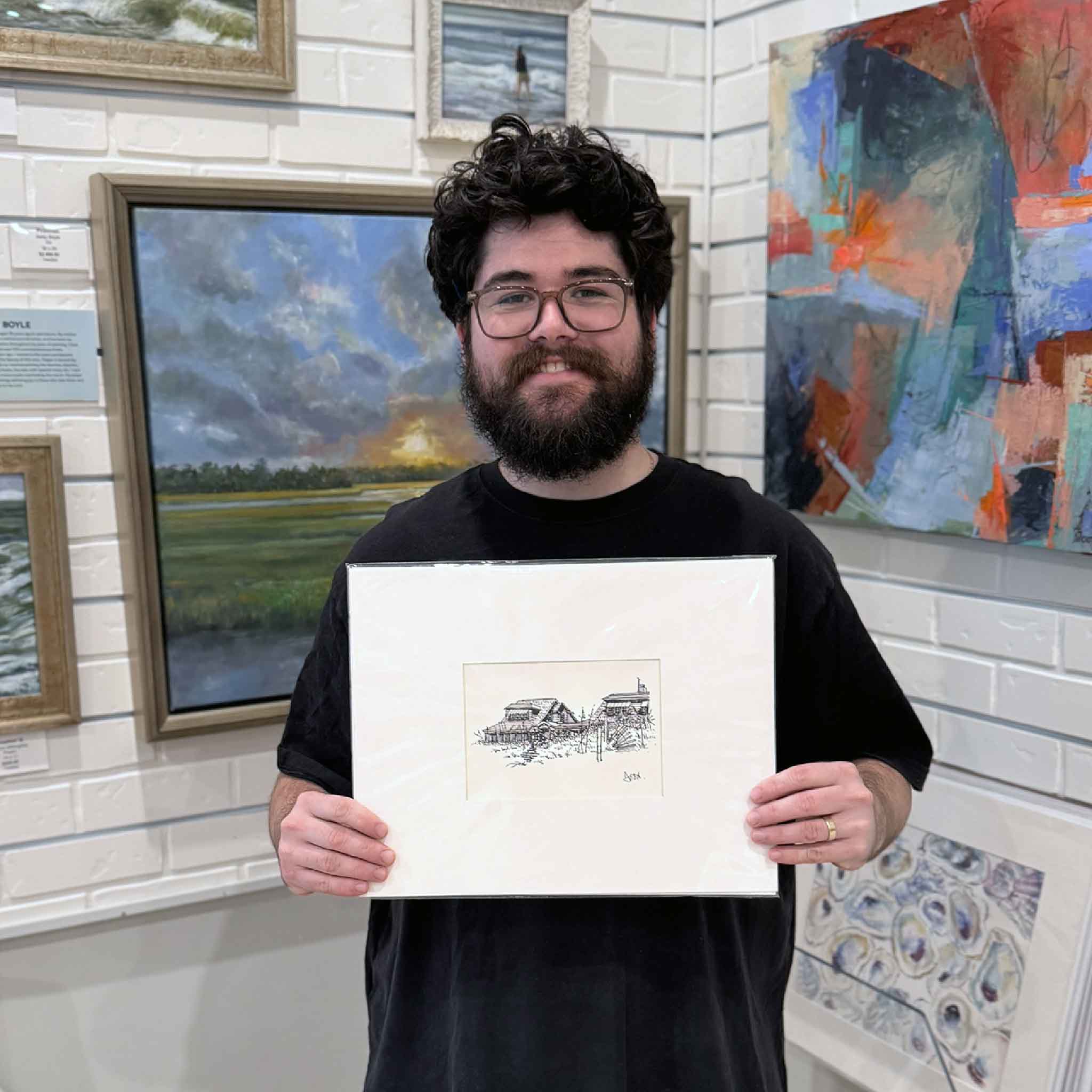 Gallery team member holding the matted Pawleys Cottages Study print by Todd Halamka inside Gray Man Gallery with coastal artwork on the walls.