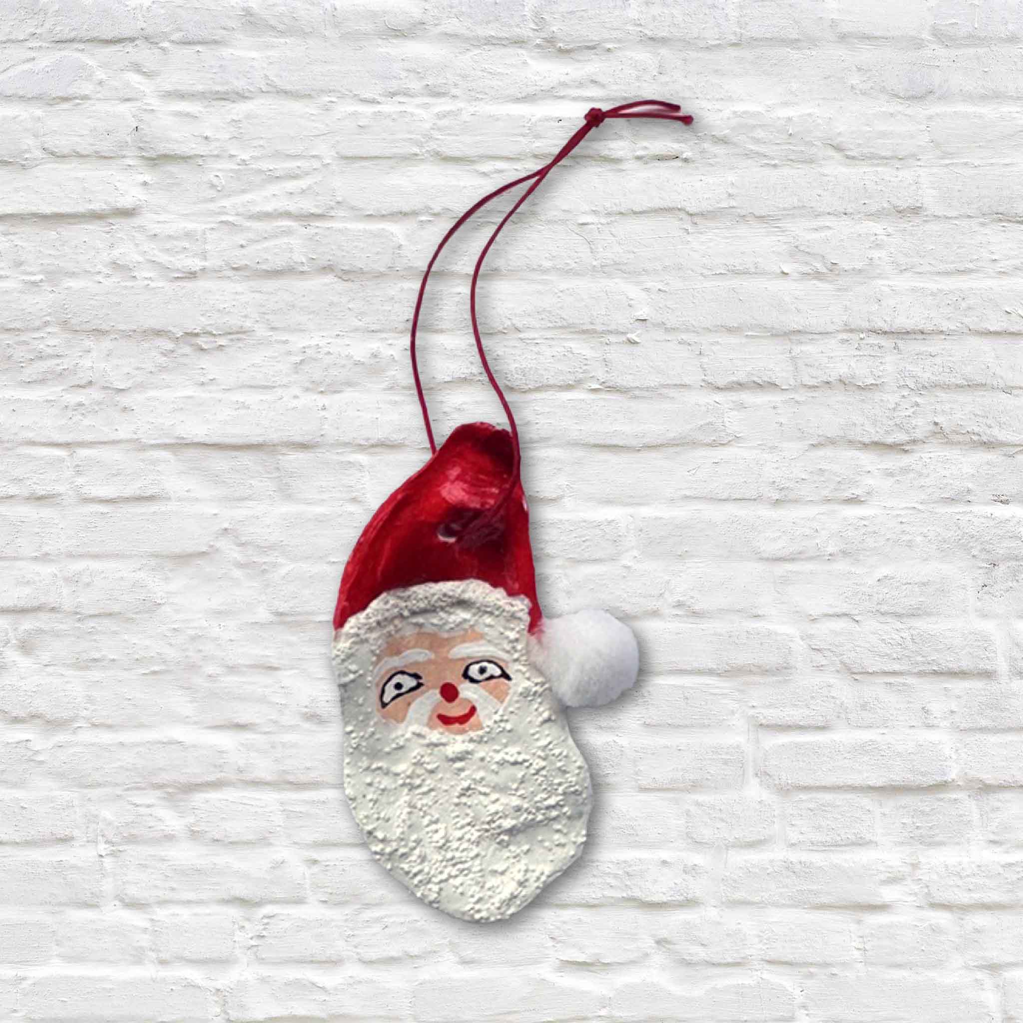 Hand-painted oyster shell Santa ornament with red hat and white beard, created by artist Tootsie Watkins.