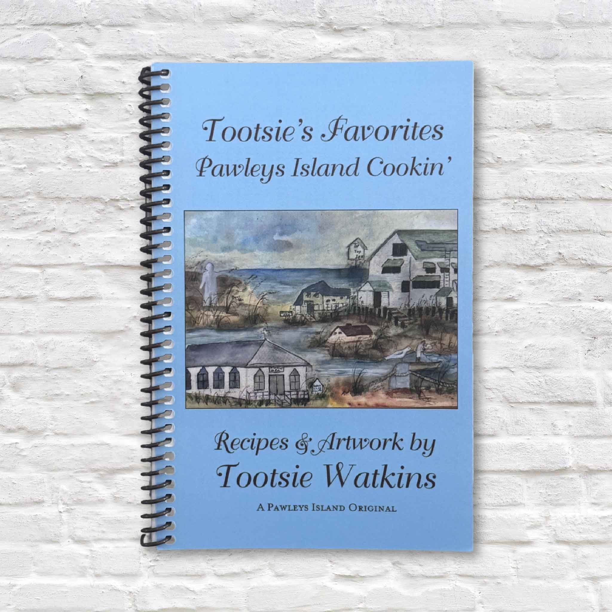 Front cover of Tootsie’s Favorites: Pawleys Island Cookin’ spiral-bound cookbook by local author and artist Tootsie Watkins, featuring Lowcountry recipes and coastal watercolor artwork, photographed at Gray Man Gallery in Pawleys Island