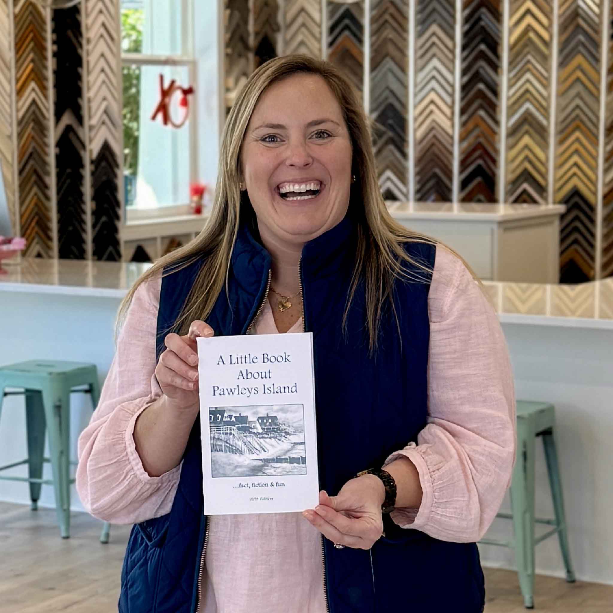 Team member holding A Little Book About Pawleys Island by local Pawleys Island author Vida Miller inside Gray Man Gallery, highlighting this popular Lowcountry history and folklore book.