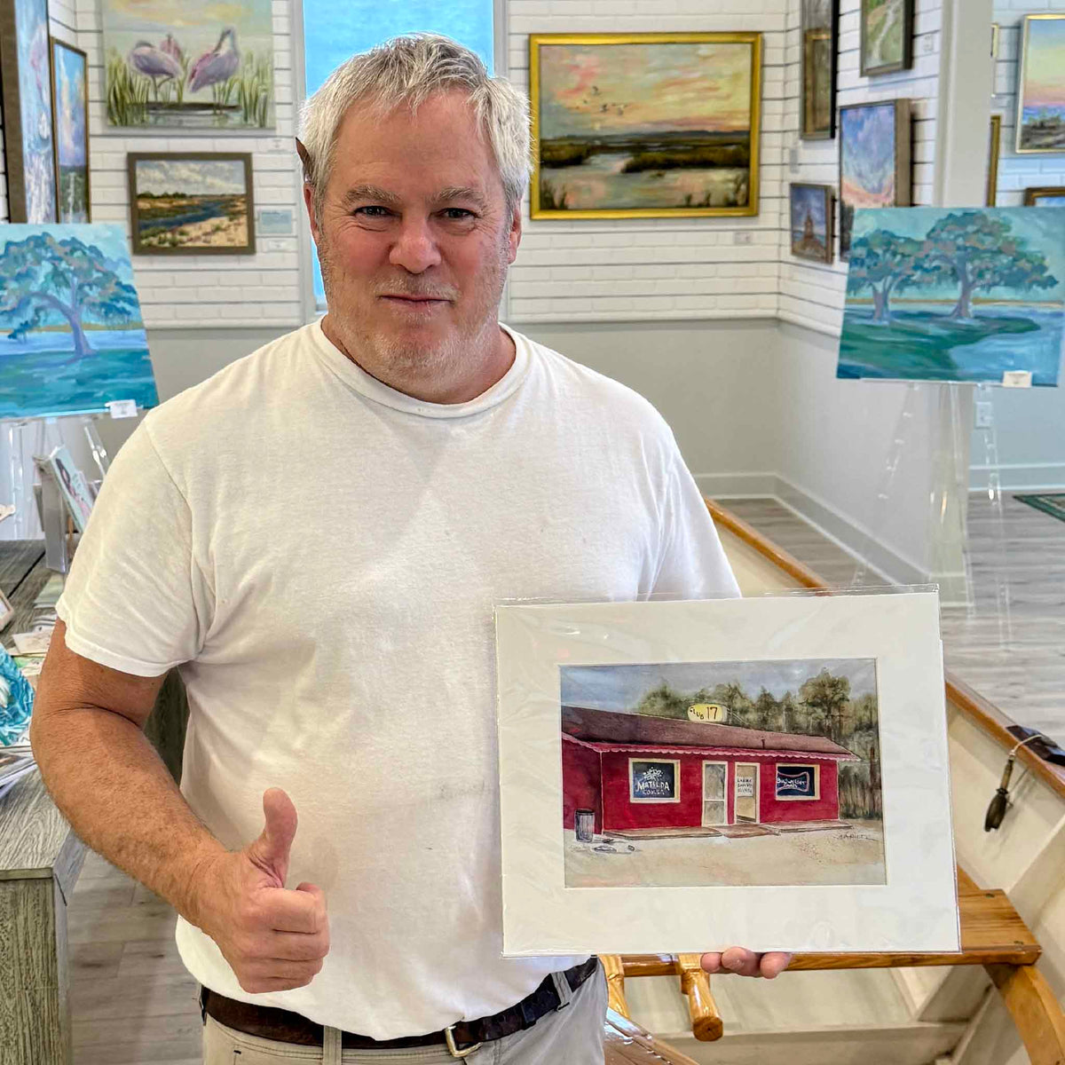 Lee, a former patron of Pawleys Island's iconic Club 17, giving a thumbs-up while displaying the 11×14 watercolor reproduction by Gray Man Gallery founder and local artist Vida Miller. The artwork captures the recognizable red building and vintage beer signs of this beloved South Carolina Lowcountry landmark, photographed at Gray Man Gallery in Pawleys Island.