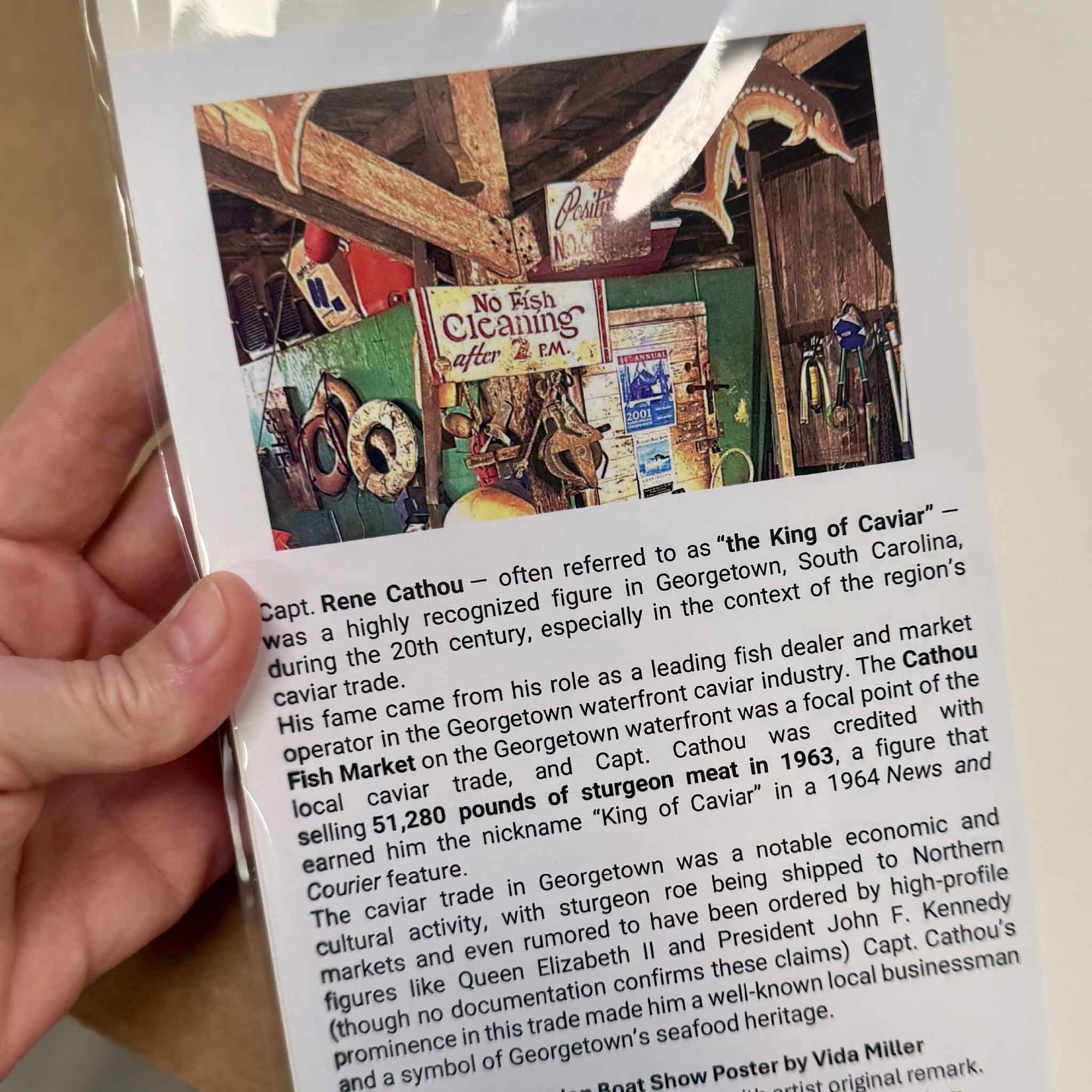 Historical information accompanying Vida Miller’s 2026 Georgetown Wooden Boat Show artist-remarqued poster, telling the story of Capt. Rene Cathou, Georgetown’s historic caviar trade, the Cathou Fish House, and the sturgeon that inspired Miller’s original hand-painted remarques, available exclusively at Gray Man Gallery in Pawleys Island.