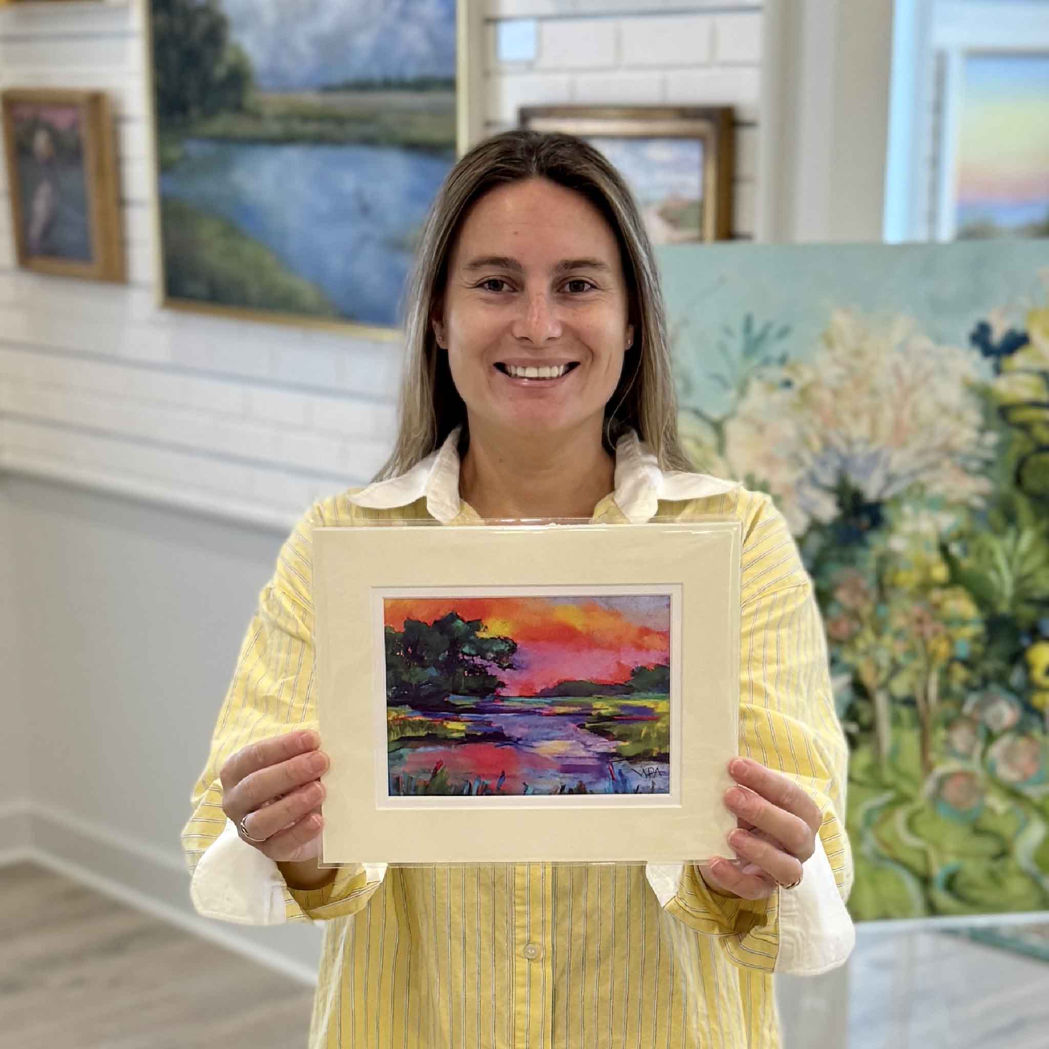Kyra holds "Marsh #1," a colorful matted Lowcountry marsh print by Pawleys Island artist Vida Miller inside Gray Man Gallery. This vibrant 8×10 artwork reproduces Miller's original pastel painting and fits any standard ready-made frame without custom framing.
