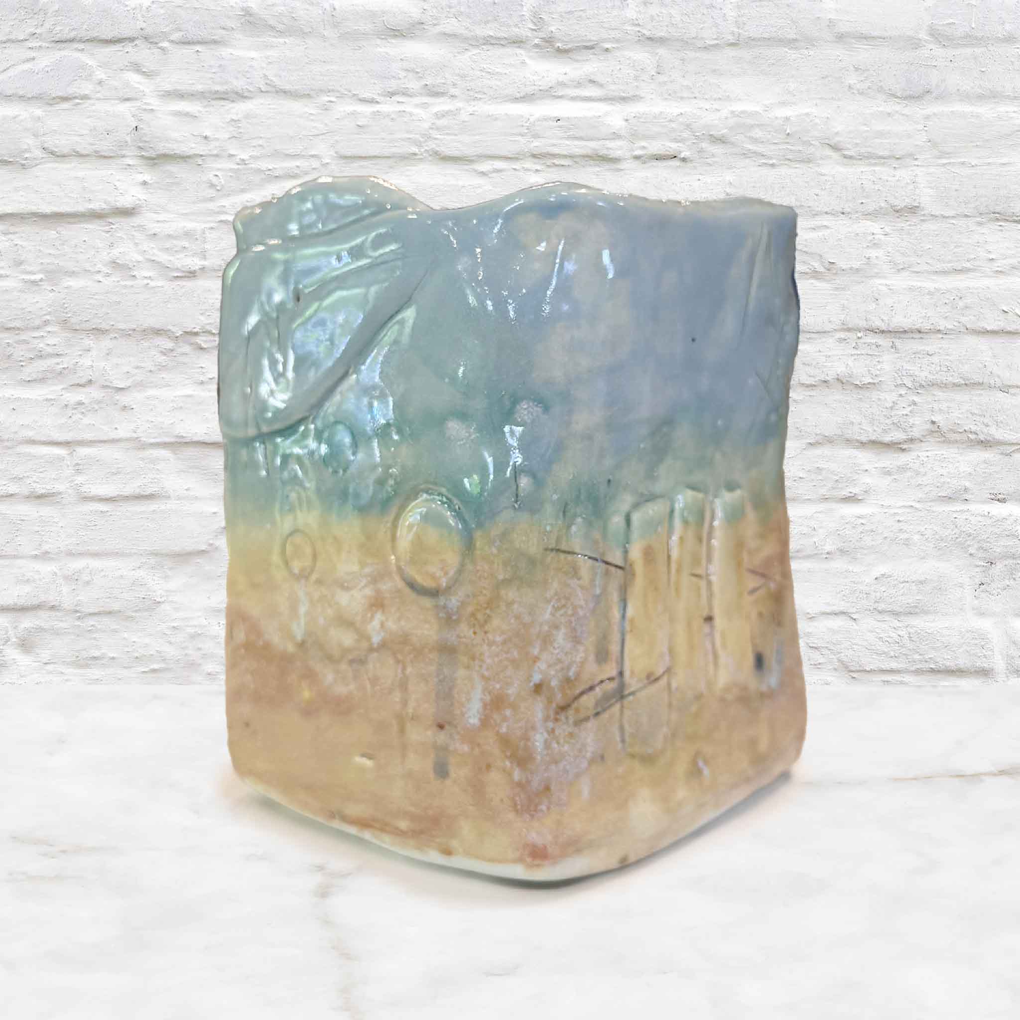 Seafoam Relic Vessel by Vida Miller handbuilt ceramic vase featuring a soft layered glaze that transitions from seafoam blue to sandy beige with subtle variations and drips, textured with organic impressions resembling shells, grasses, and coastal elements, with an irregular sculpted rim and natural form, photographed at Gray Man Gallery in Pawleys Island, South Carolina