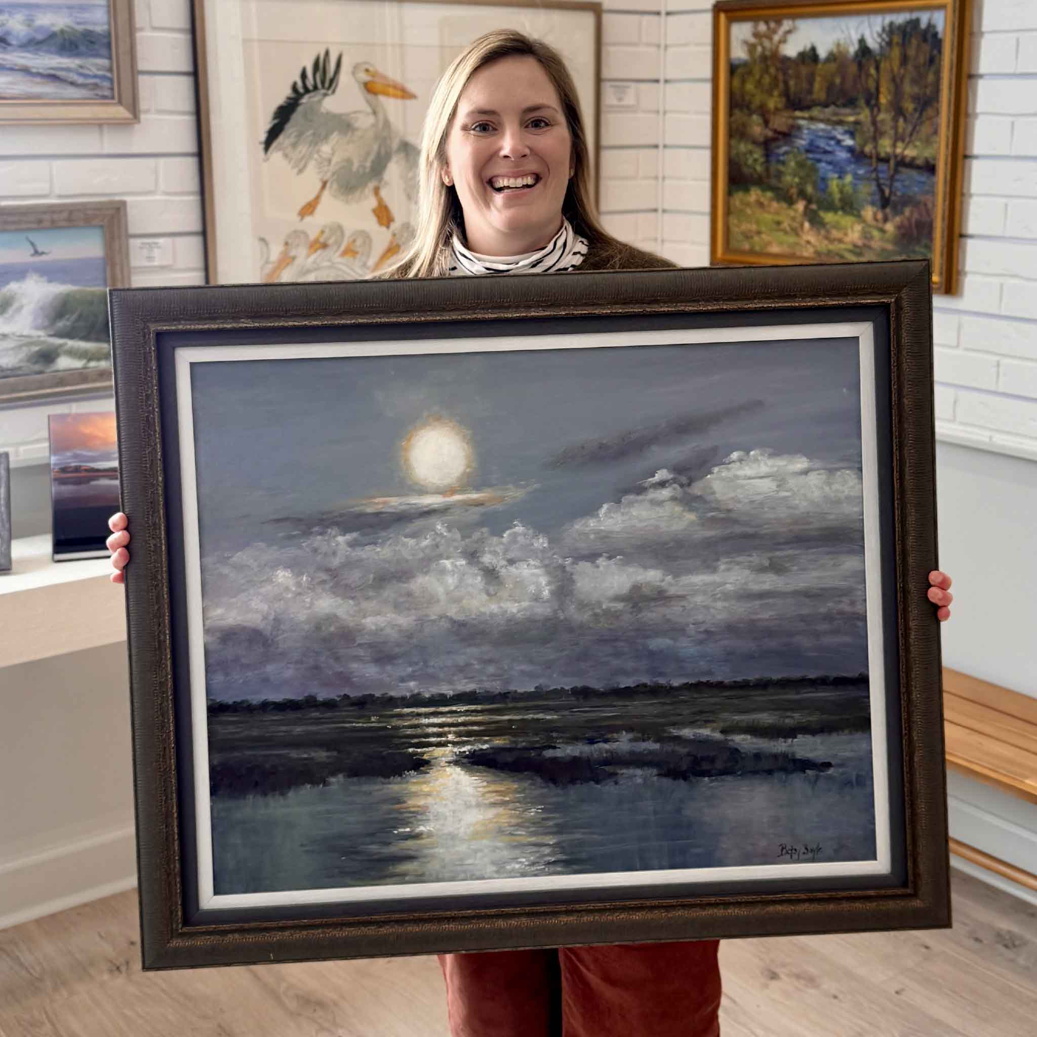 Gray Man Gallery team member Bordy holding “Watching,” a 24x36 original acrylic egret painting by local Lowcountry artist Betsy Boyle, professionally framed and displayed inside Gray Man Gallery in Pawleys Island, South Carolina