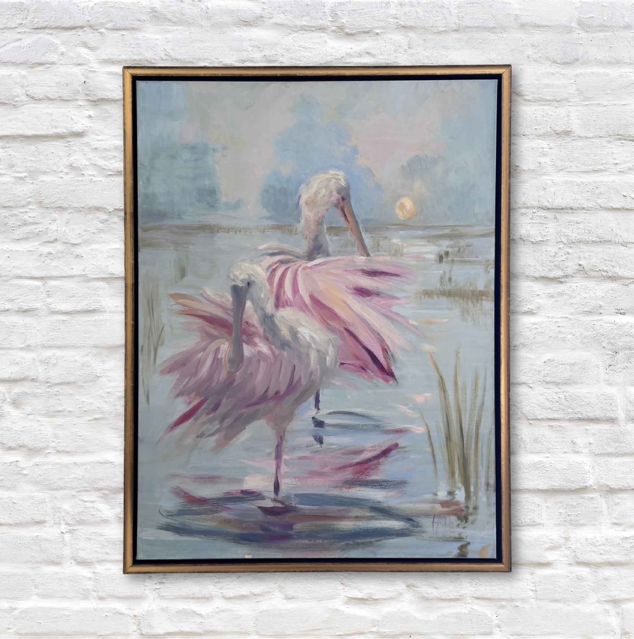 Framed painting of a roseate spoonbill in a pond with a sunset background on a white brick wall.
