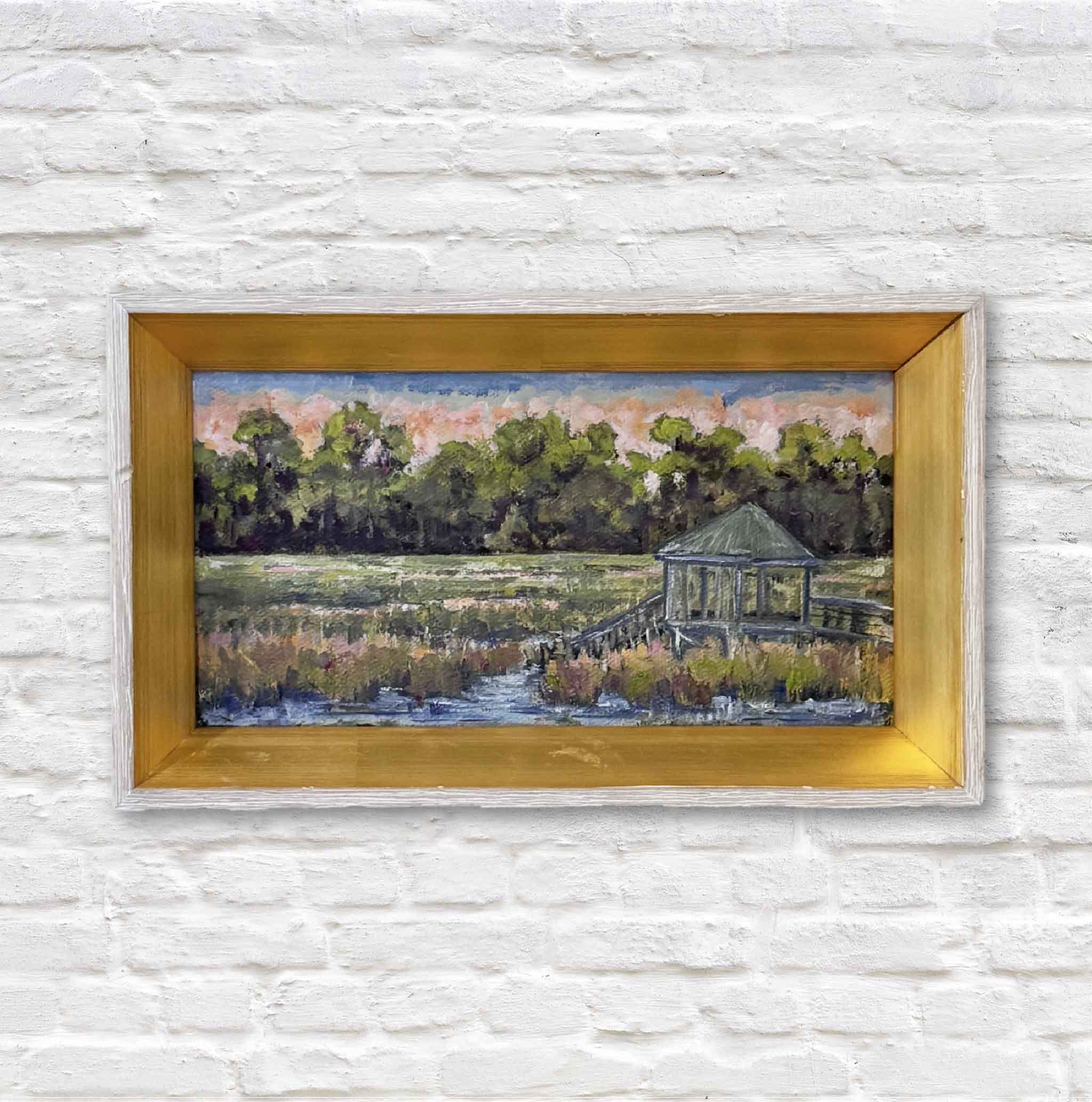 Framed painting of a landscape with a gazebo on a white brick wall