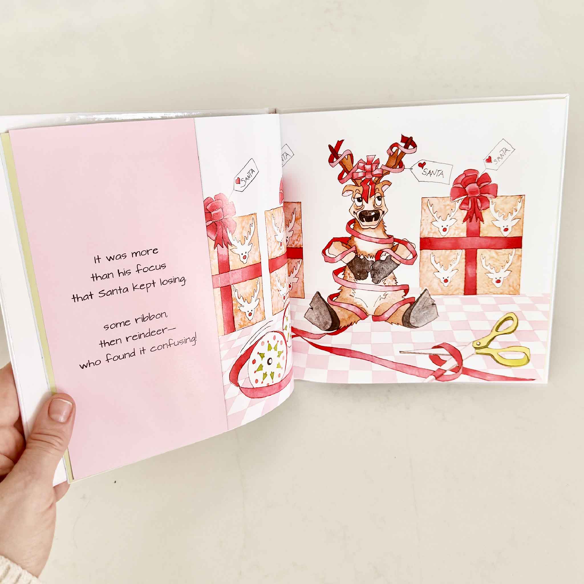 Open book with Christmas-themed illustrations of a reindeer and presents on a pink background.