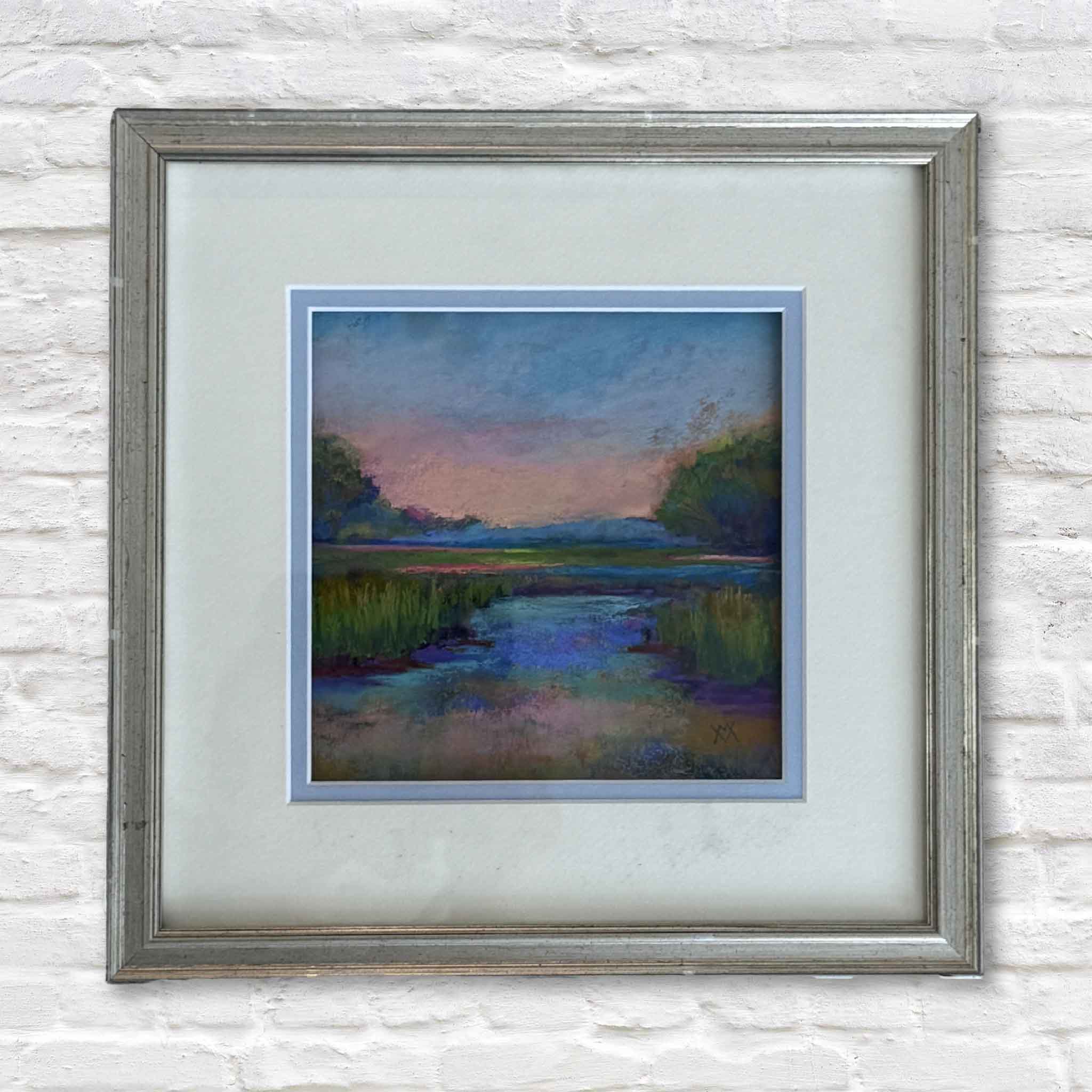 Framed painting of a landscape with a sunset over water on a textured white wall.