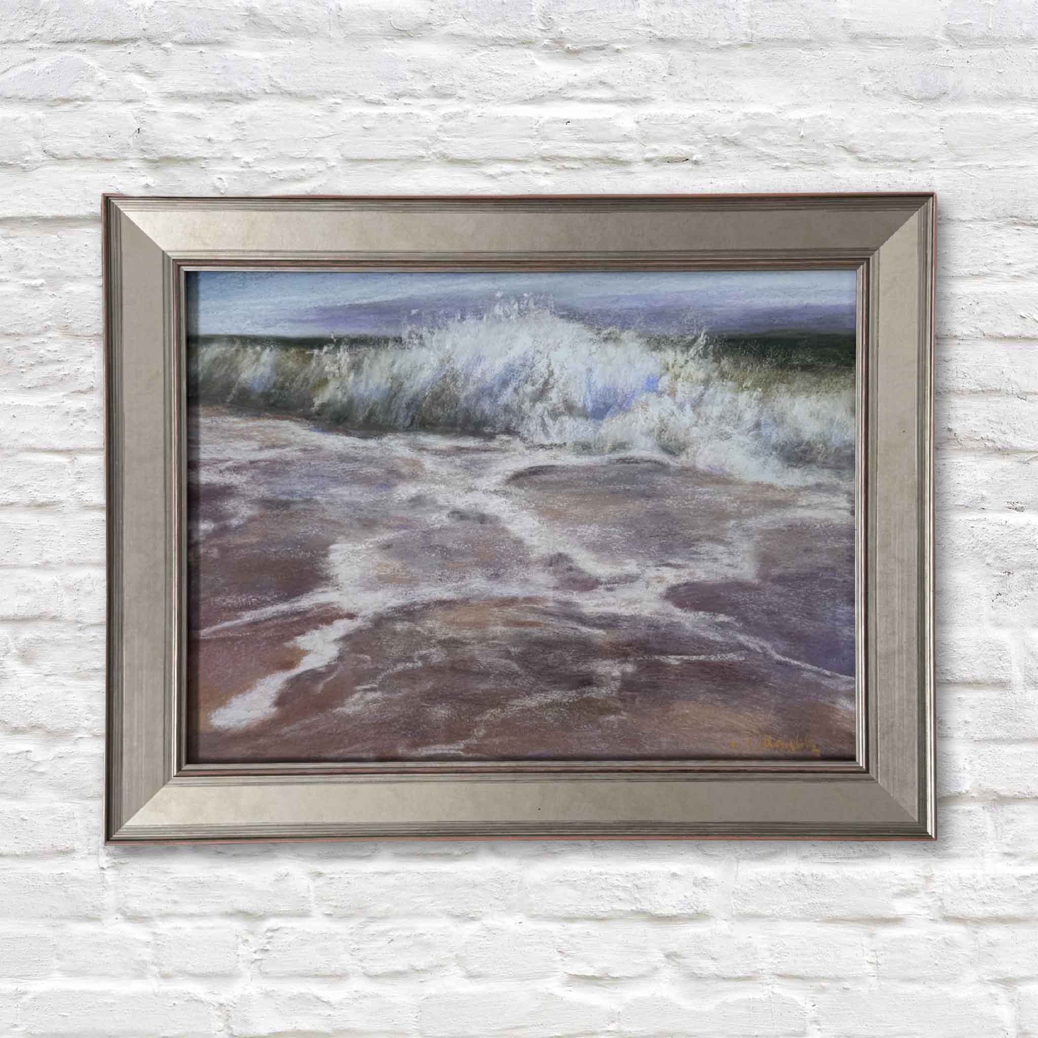 Framed painting of a wave crashing on a beach against a white brick wall.