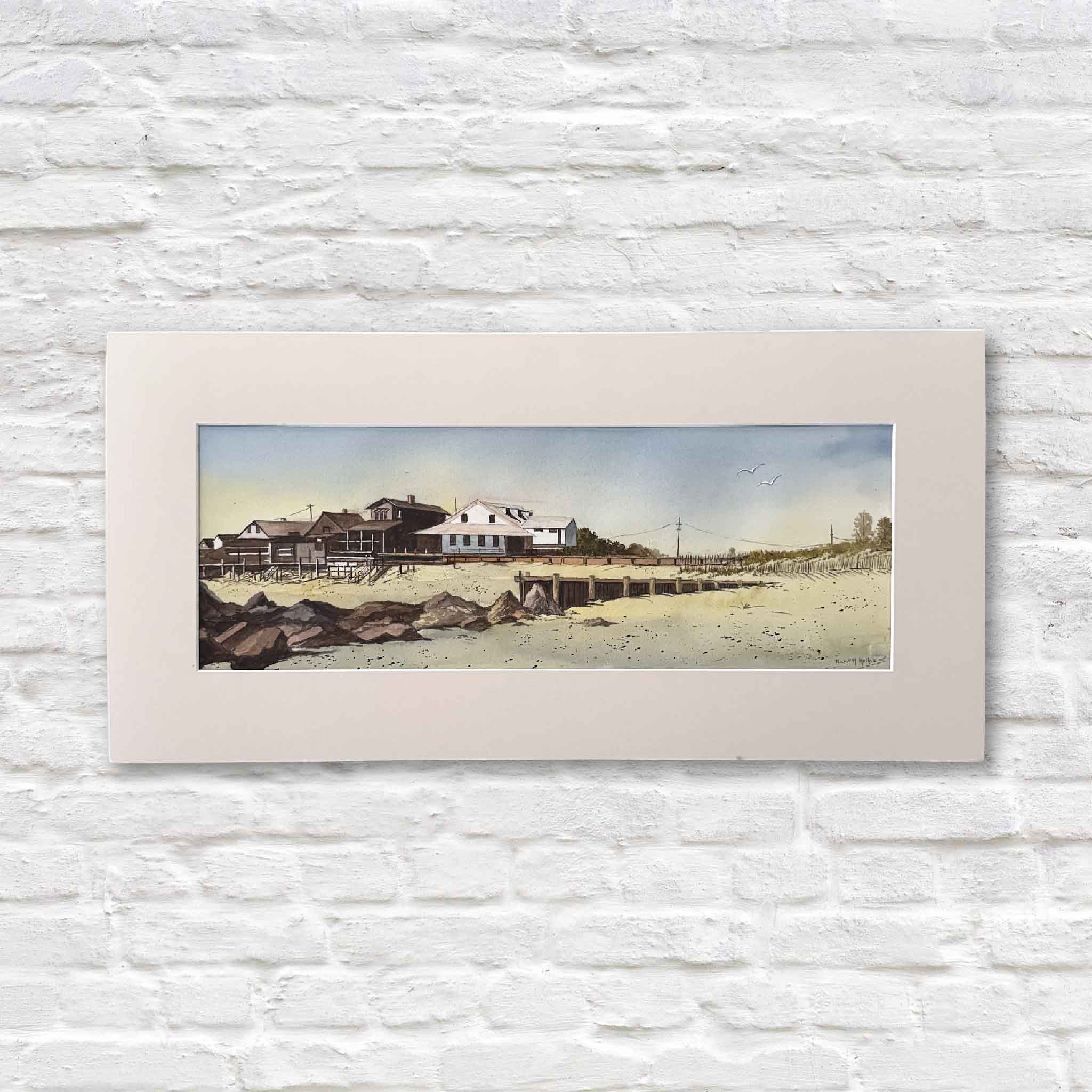 matted artwork of a Pawleys beach scene with houses on a white brick wall.