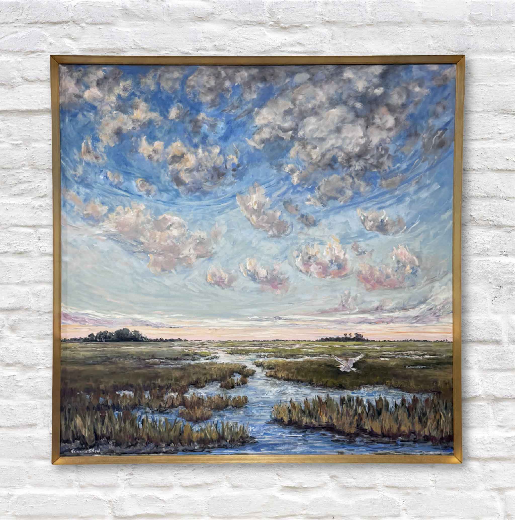 Framed painting of a landscape with a river and sky on a white brick wall.
