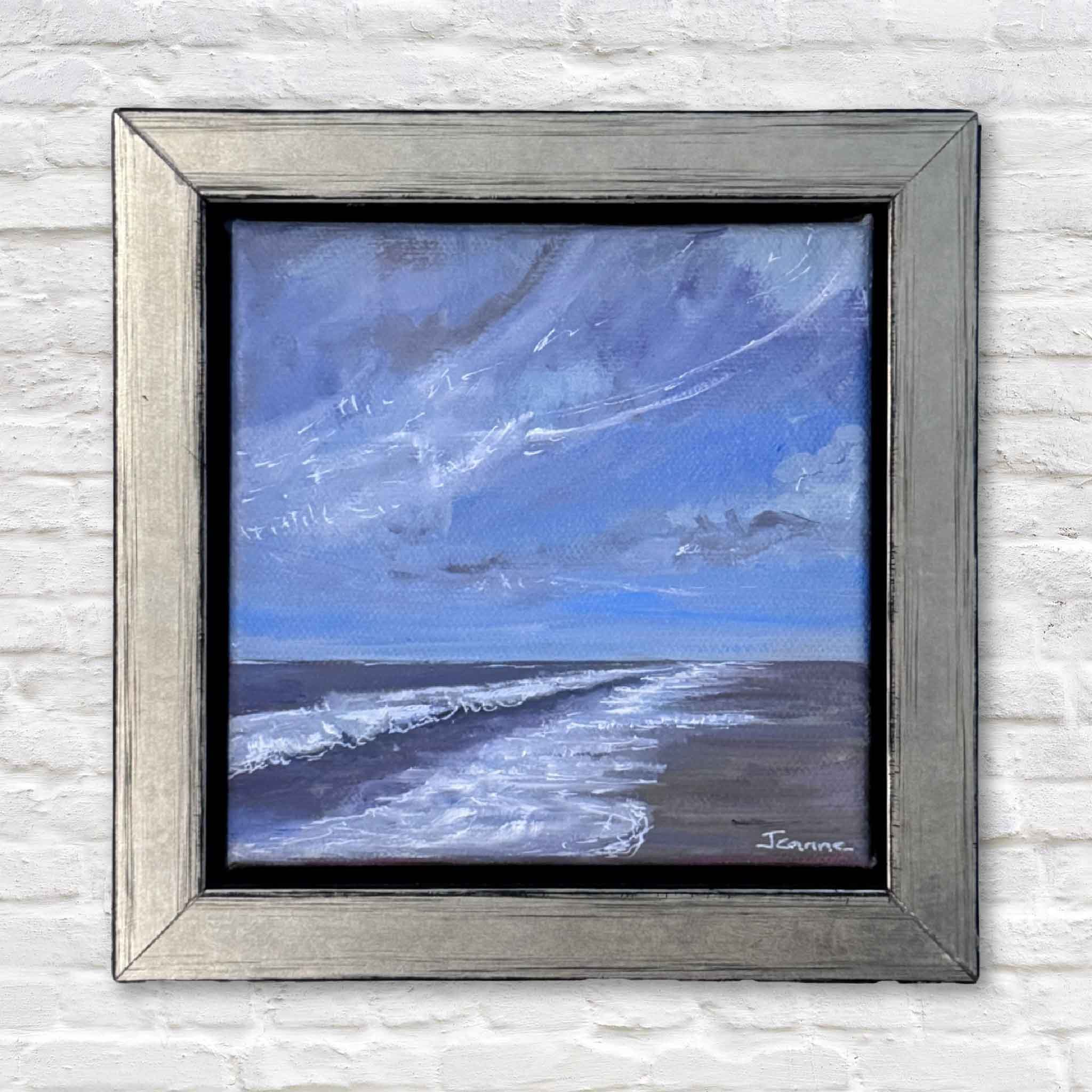 Framed painting of a coastal scene with blue sky and white waves on a textured wall.