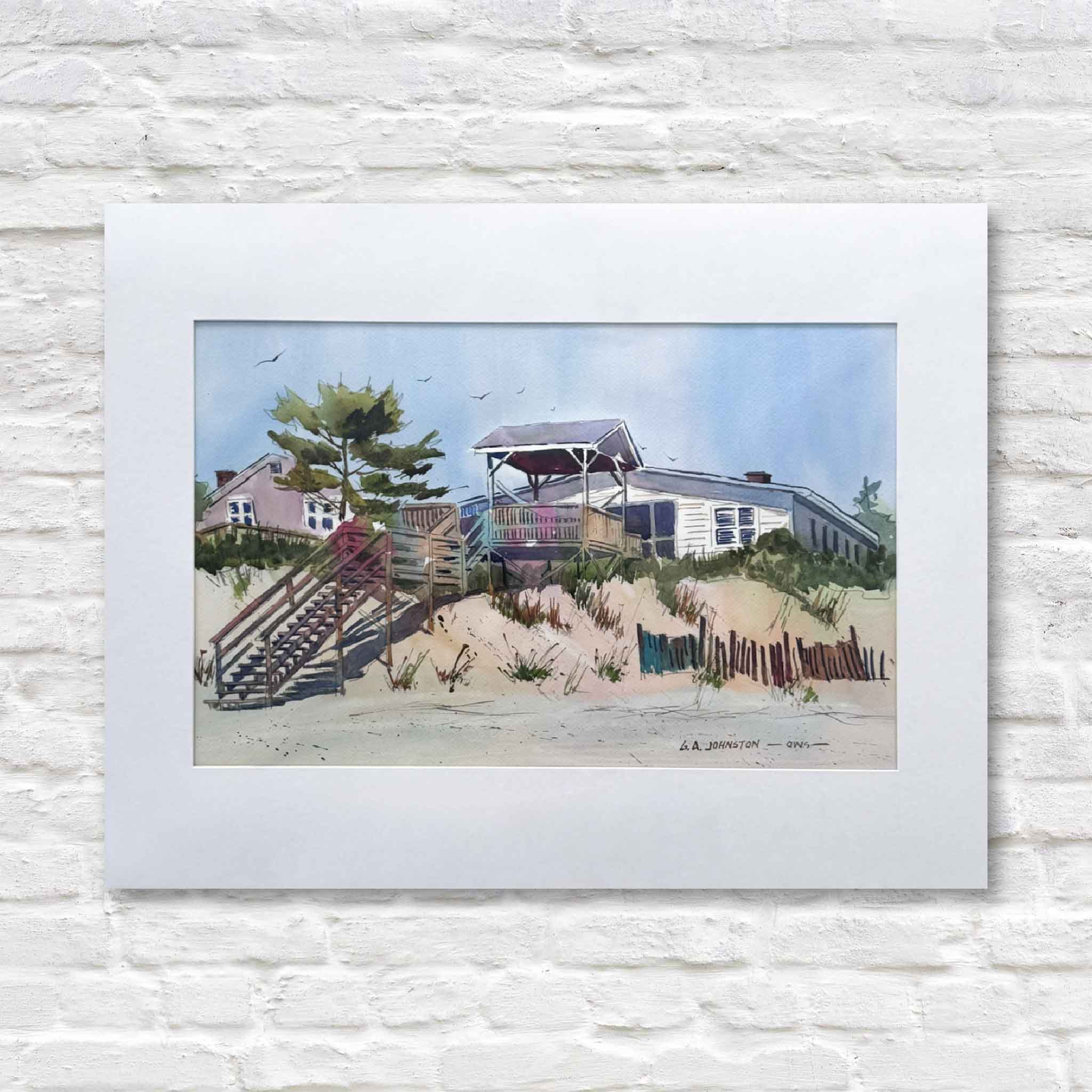 matted original artwork of a pawleys beach scene with houses and sand dunes on a white brick wall.