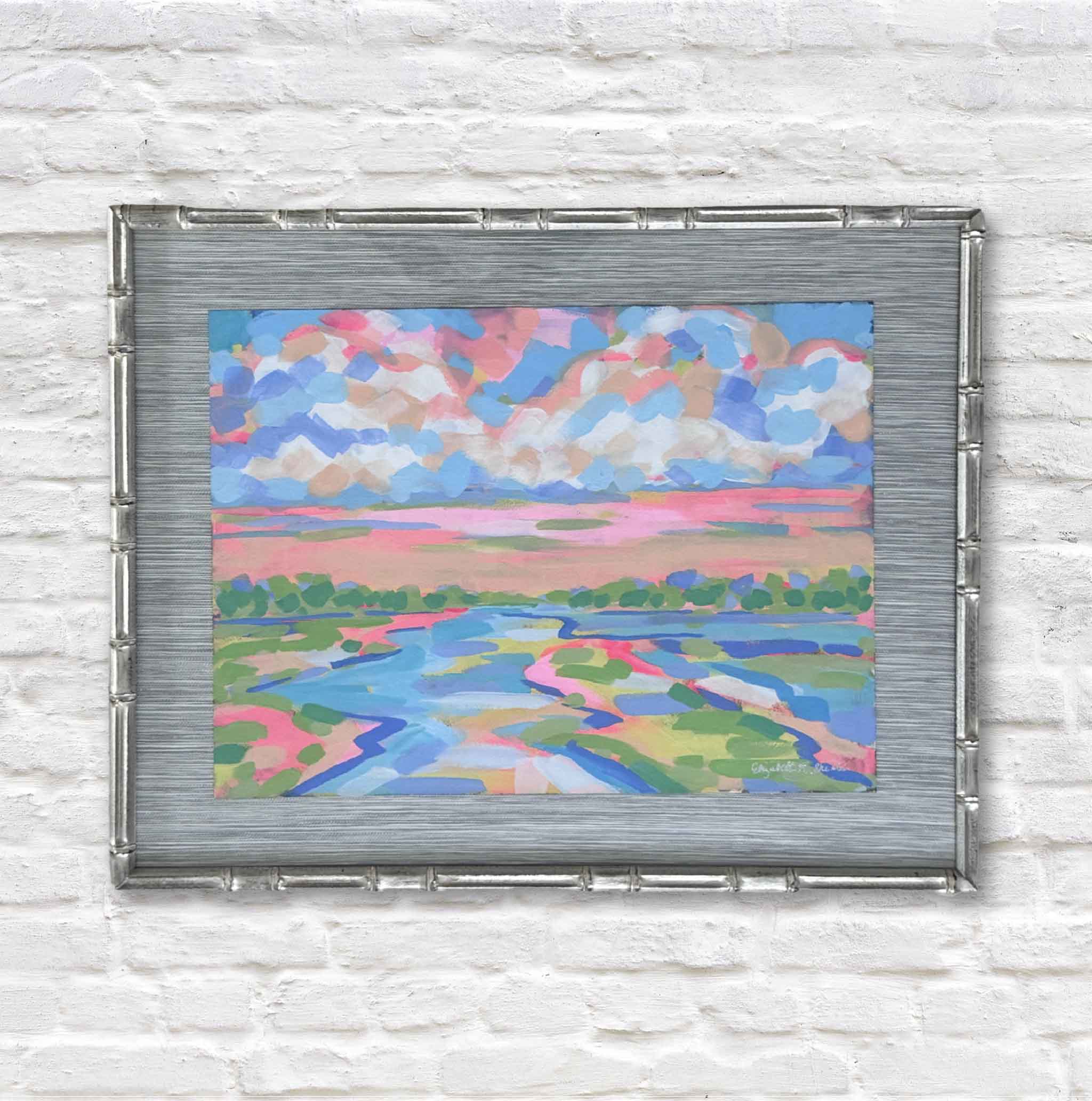 Colorful abstract landscape painting in a metallic frame on a white brick wall.